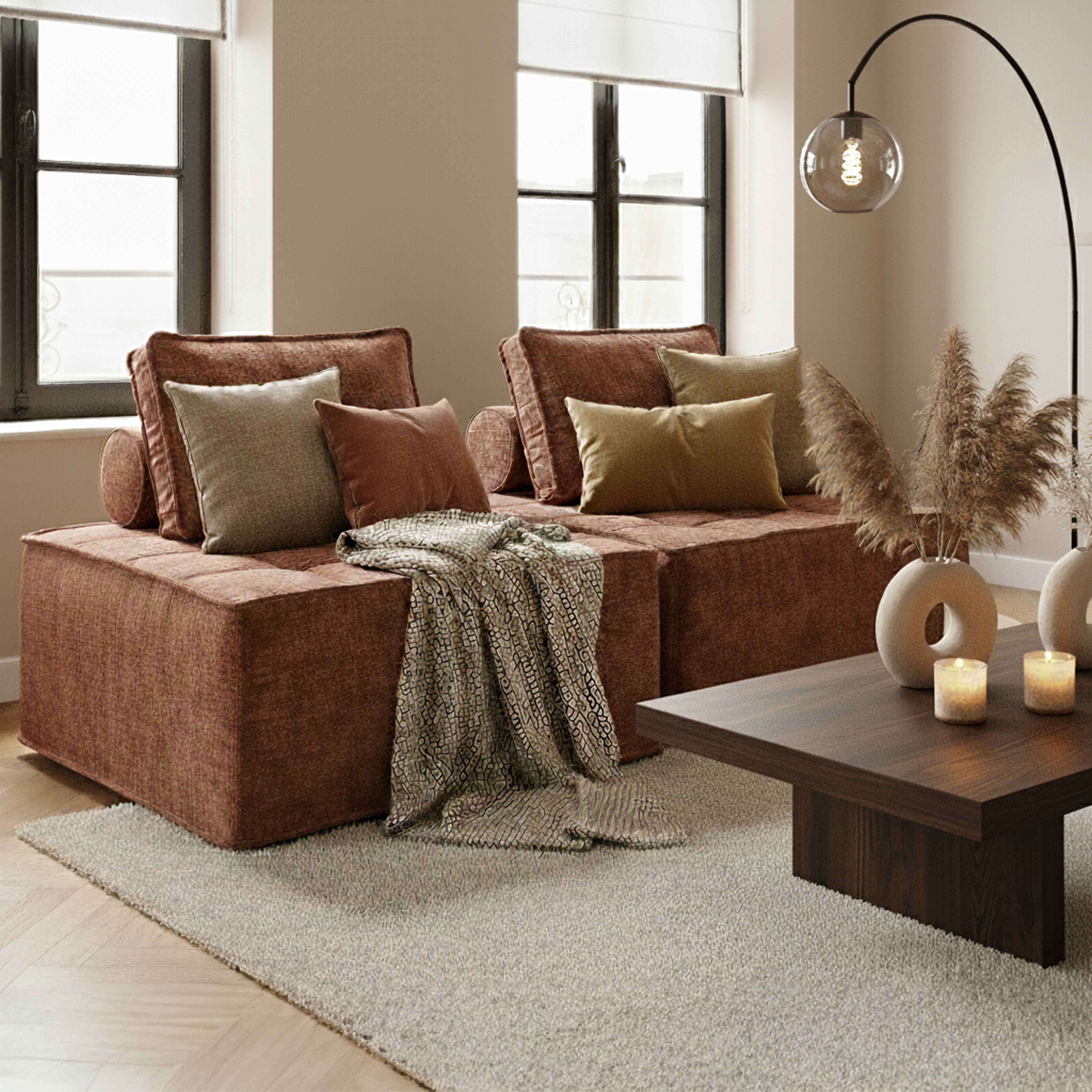 Ein modernes Wohnzimmer mit braunem Sofa, Kissen, Decke, Holztisch, Kerzen und Stehlampe.