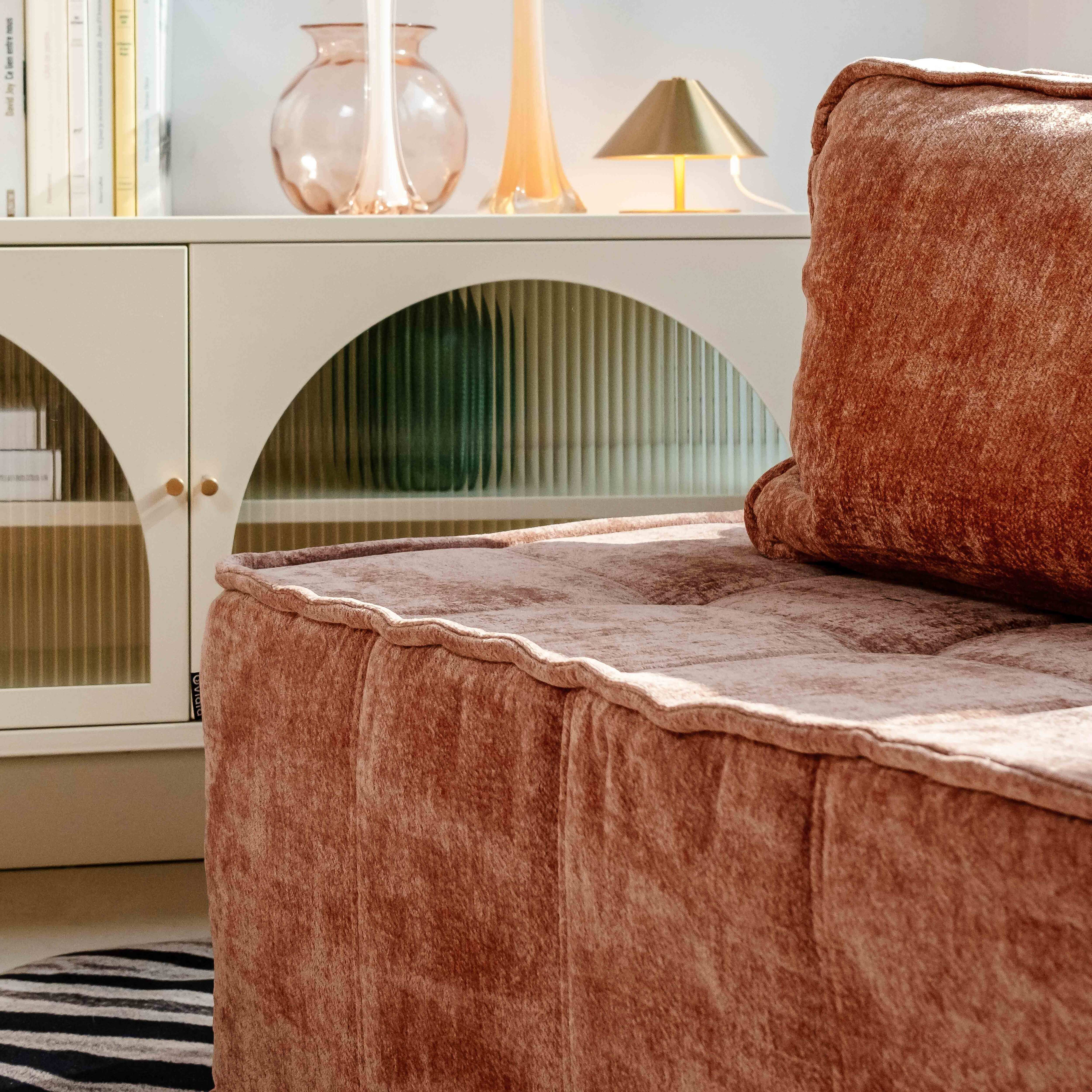Nahaufnahme eines rosabraunen Sofas, eines Schranks mit Glastüren und einer kleinen Lampe.