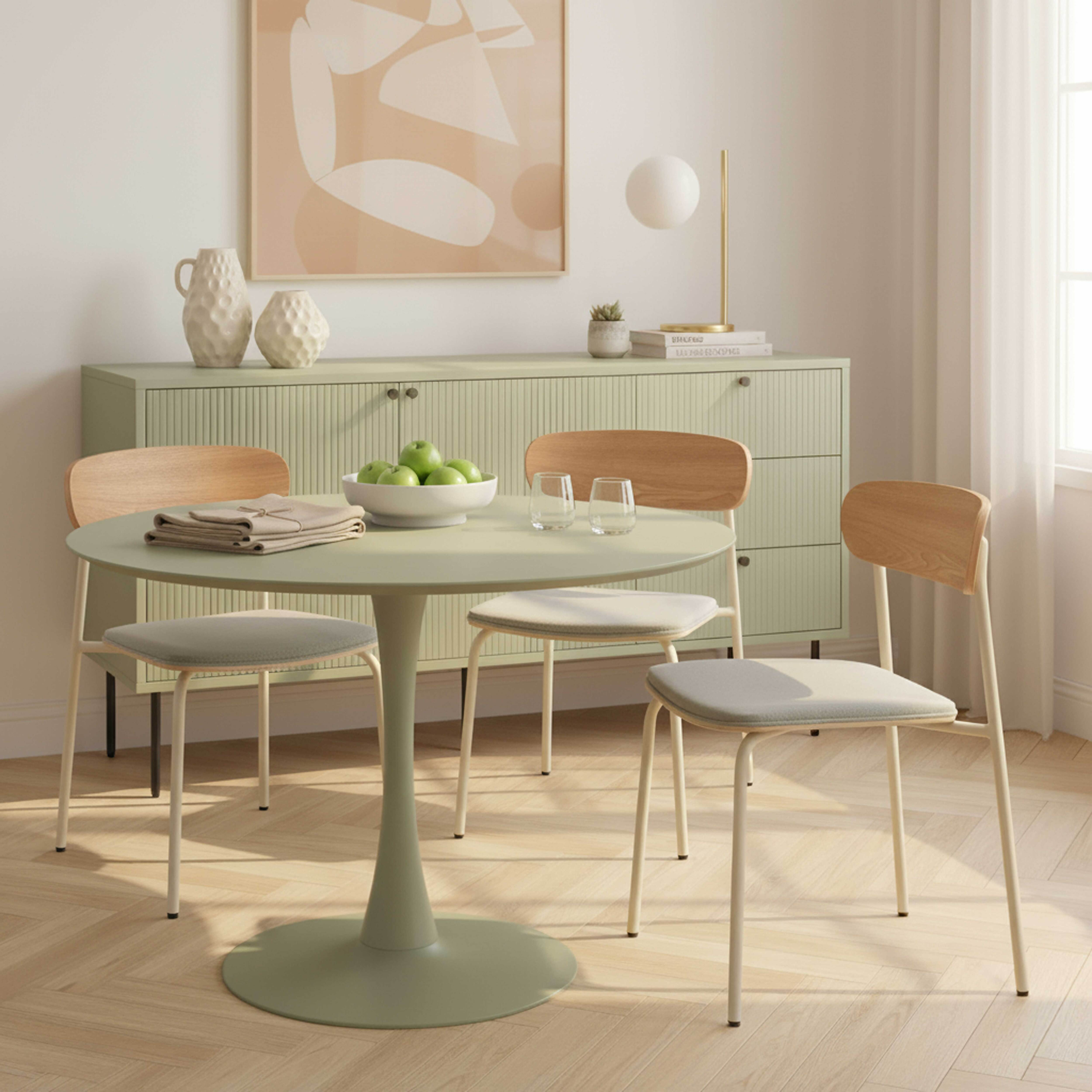 Esszimmer mit grünem Tisch, Stühlen, Schrank und Kunstwerken. Grüne Äpfel in einer Schüssel auf dem Tisch.
