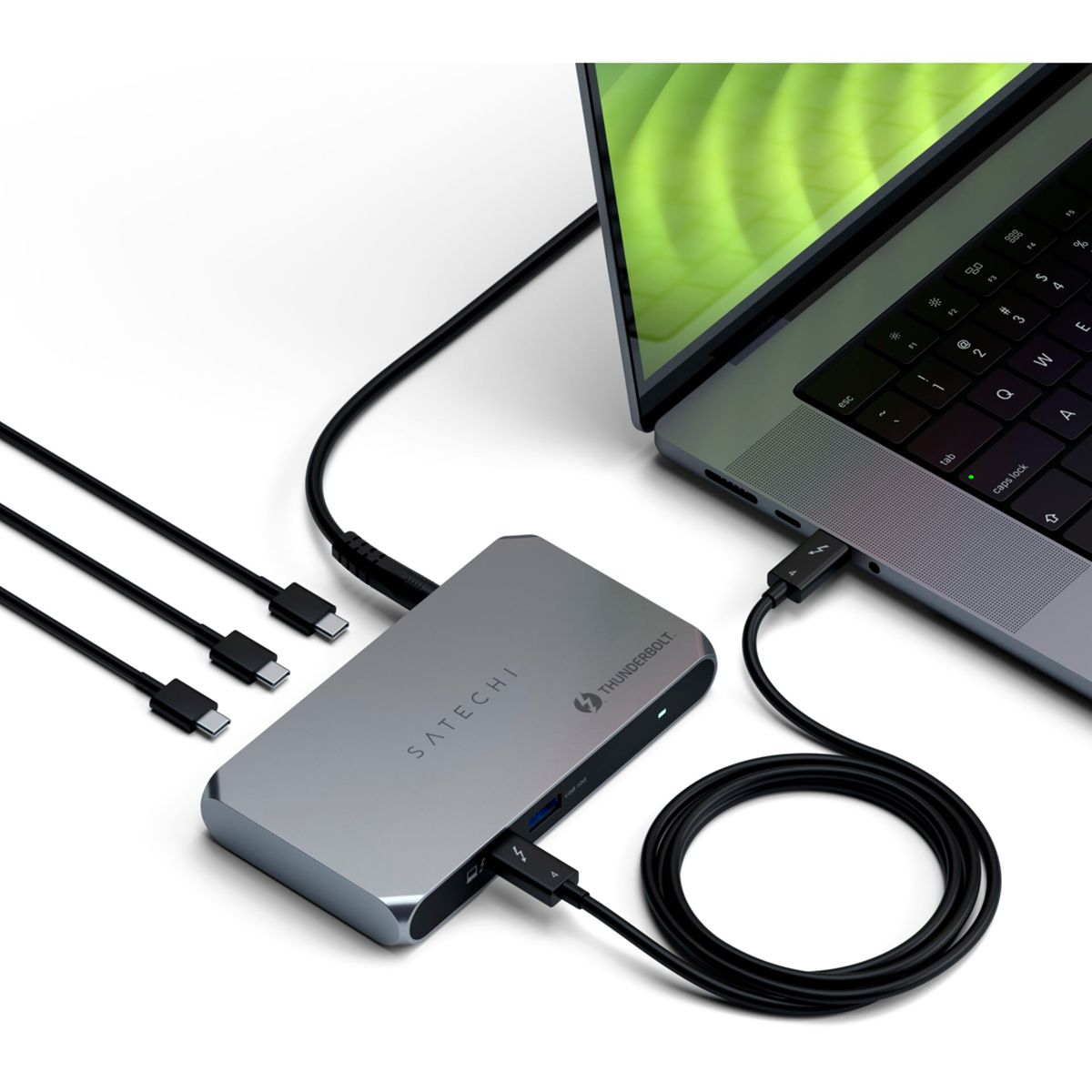 Un hub Thunderbolt Satechi argentato collegato a un laptop. Cavi neri collegati all'hub e al laptop, su una superficie bianca.