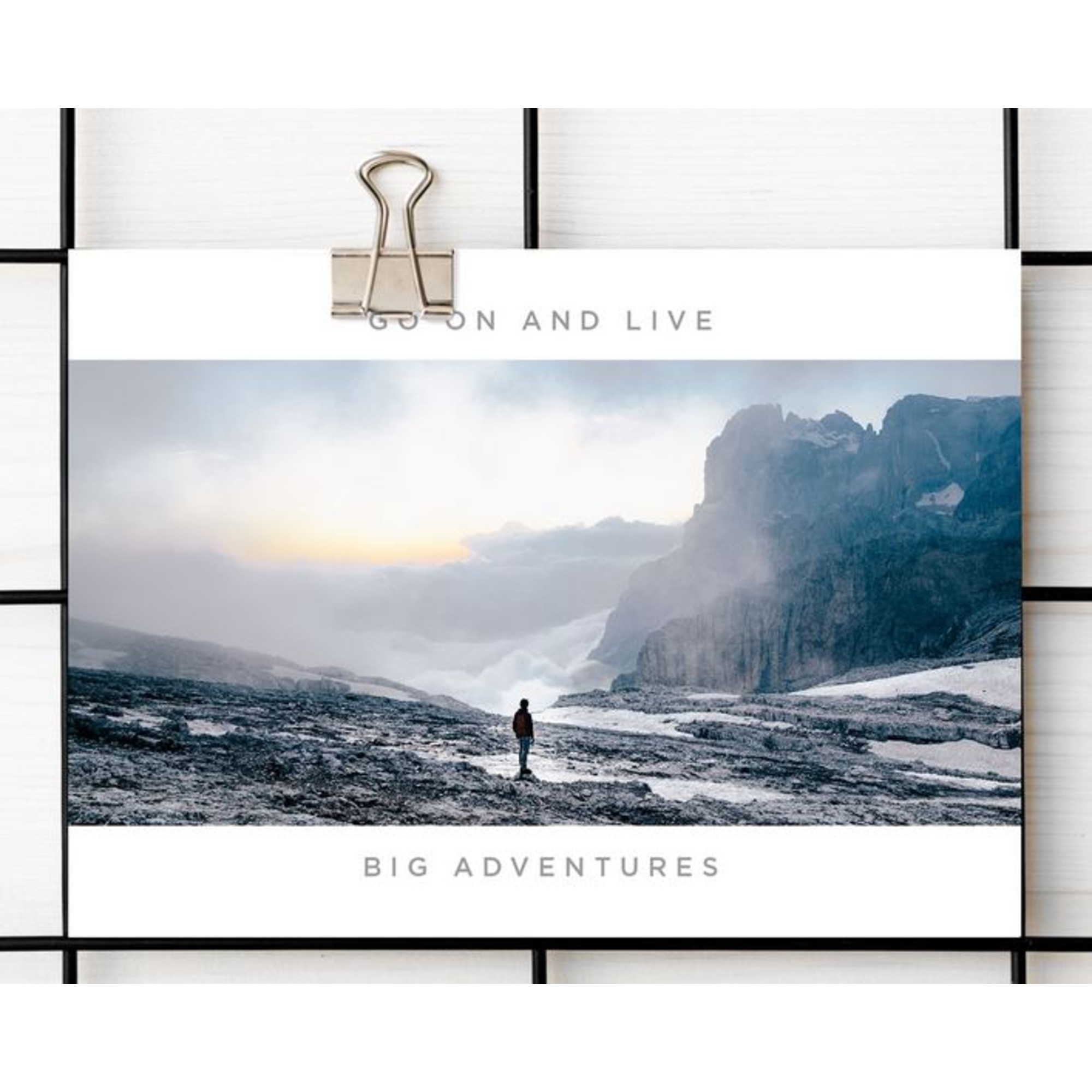 Eine Person steht auf einem felsigen Berg, mit Blick auf ein bewölktes Tal und hoch aufragende Berge. Der Text lautet 'Go on and live'.