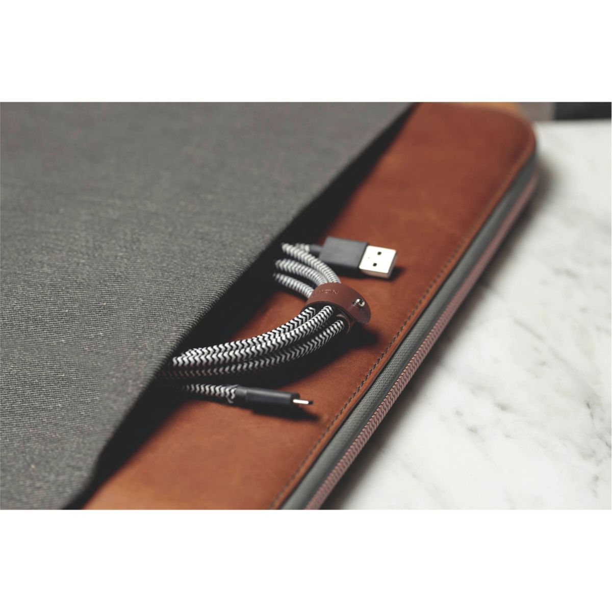 Eine braune Ledertasche mit einer grauen Stofftasche, die ein Ladekabel mit einem schwarz-weißen Muster und einem USB-Anschluss enthält.