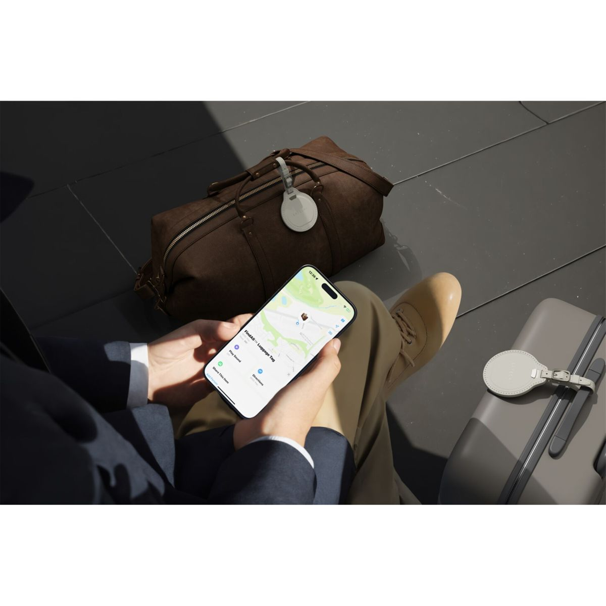Eine Person hält ein Telefon mit einer Karte, Gepäck und einem Gepäckanhänger. Eine braune Tasche und ein Koffer sind ebenfalls sichtbar.