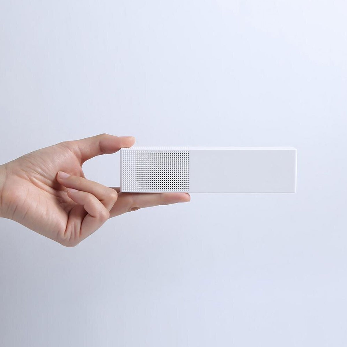 Dłoń trzyma białe prostokątne urządzenie. Urządzenie ma perforowaną część po lewej stronie i gładką powierzchnię po prawej.