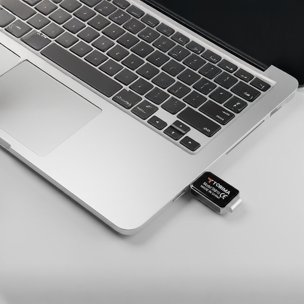 Siyah klavyeli bir dizüstü bilgisayar ve takılı bir USB sürücü. USB sürücü siyah üzerine beyaz yazılı, dizüstü bilgisayar gümüş rengi.