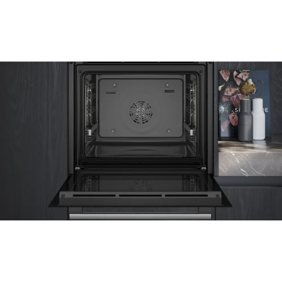 Een open oven met interieurdetails, deur op een kier. Daarnaast kookboeken, zout- en pepermolens op een aanrecht.