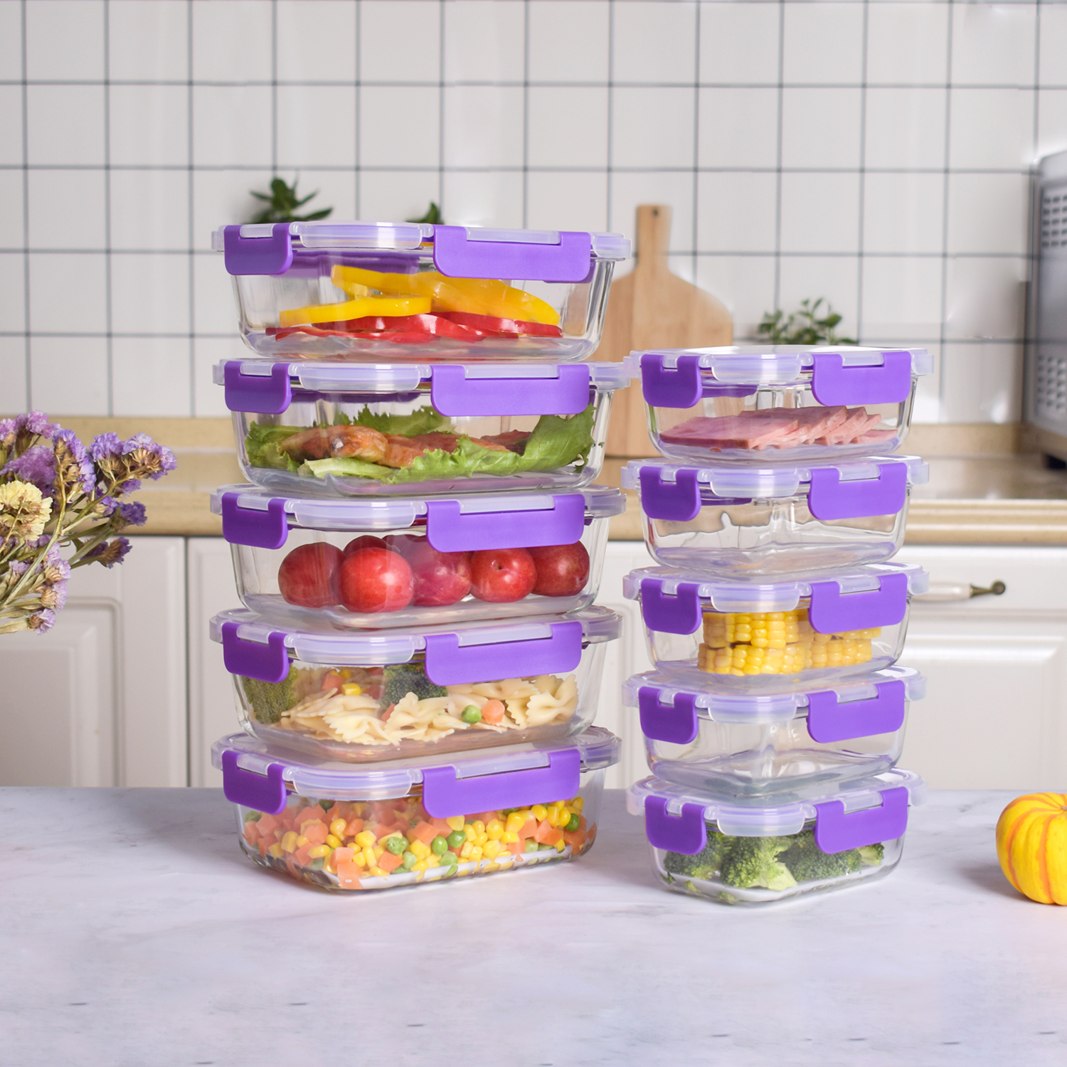 Contenedores de vidrio con tapas moradas, llenos de alimentos como verduras, carne y frutas, apilados en un mostrador blanco.