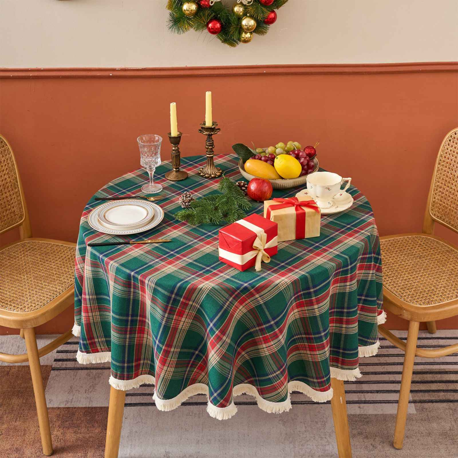 Ein runder Tisch, der für einen festlichen Anlass gedeckt ist. Er hat eine grün karierte Tischdecke, Obst, Geschenke und Kerzen.