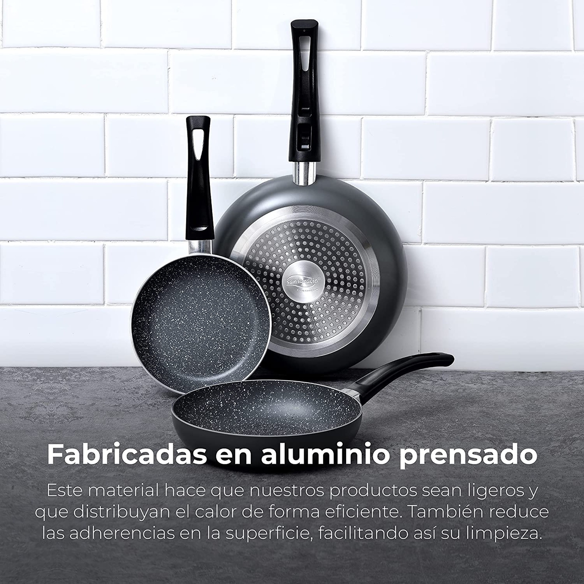 Tres sartenes antiadherentes con mangos negros sobre una superficie gris, fondo de azulejos blancos. Texto: 'Fabricadas en aluminio prensado'.