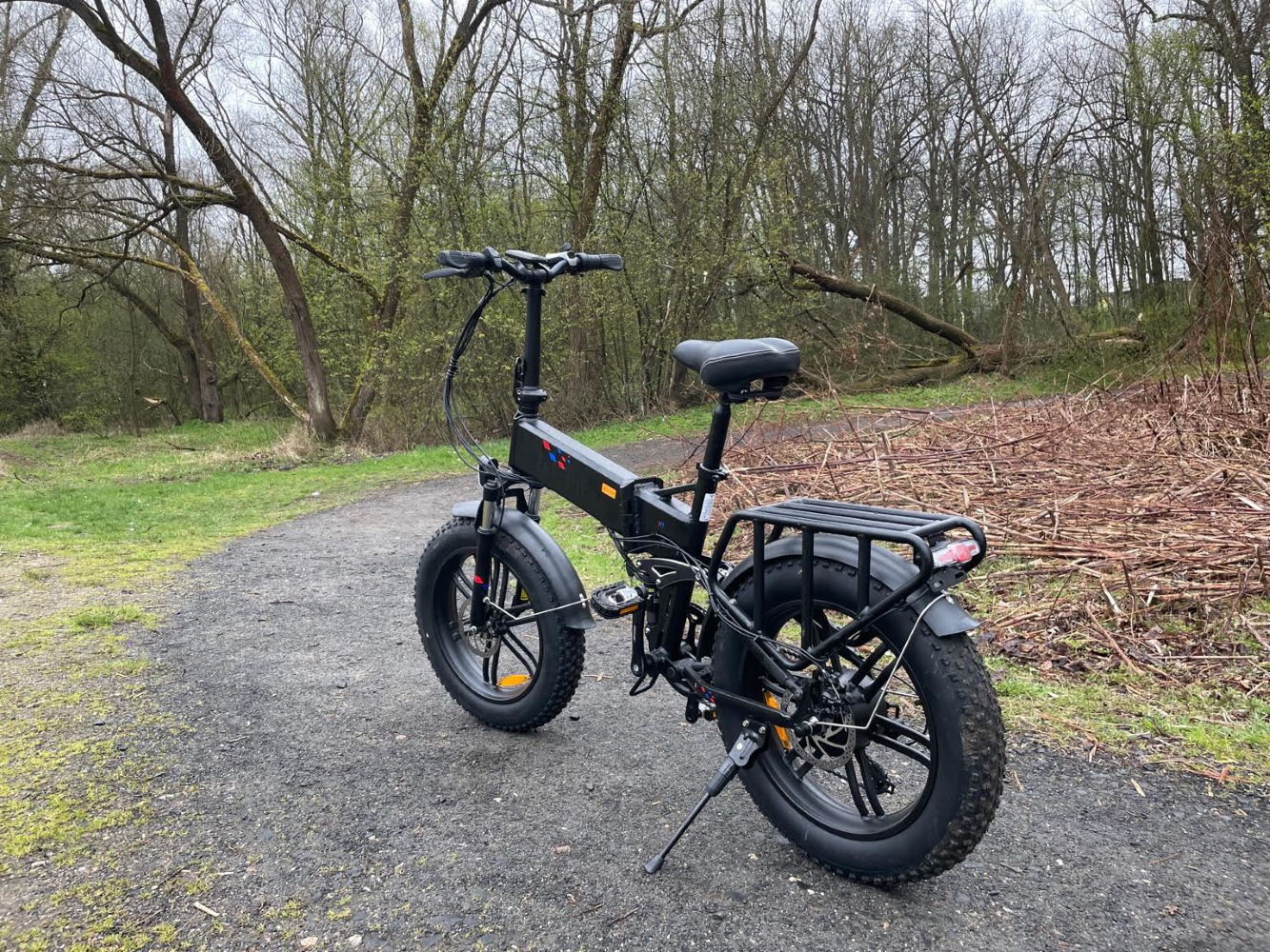 Bicicleta eléctrica negra en un camino de grava. Árboles al fondo. Día nublado.
