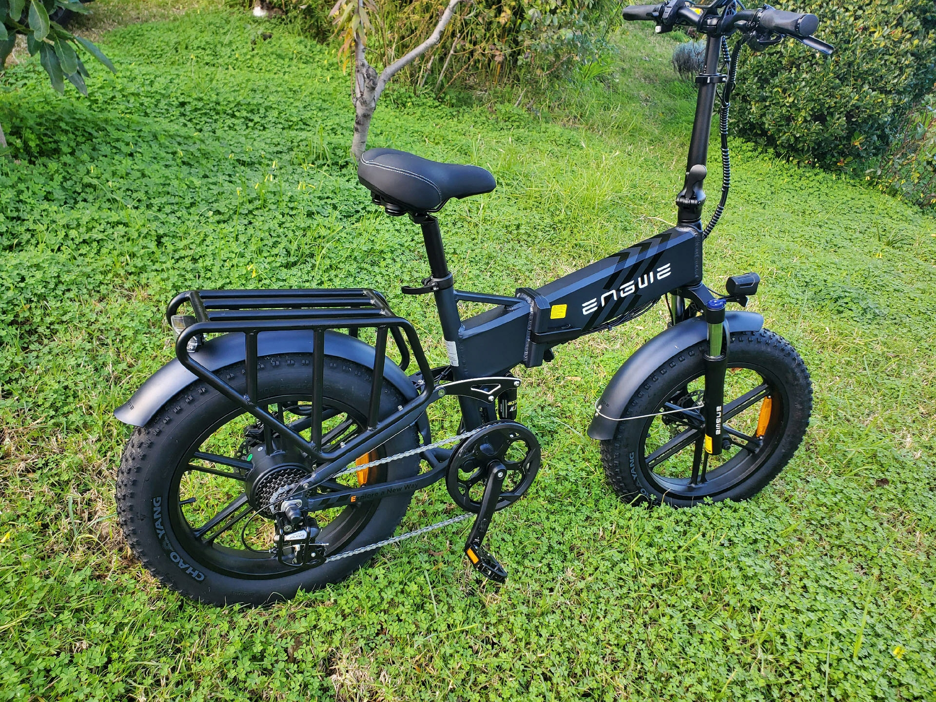 Una bicicleta eléctrica Engwe negra se encuentra sobre hierba verde, con neumáticos gruesos y un portaequipajes trasero.