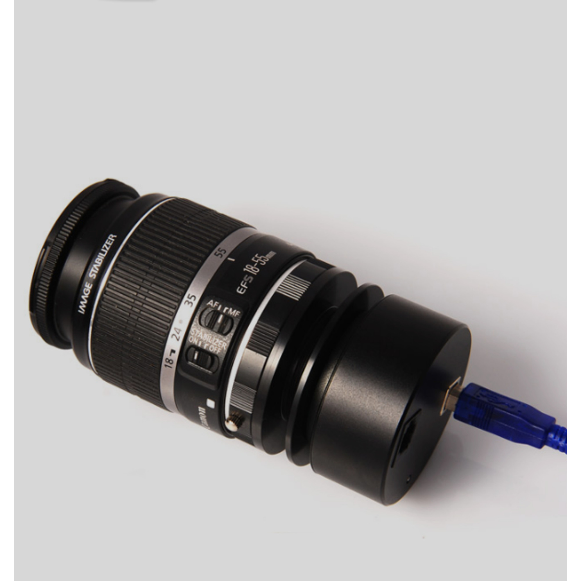 Ein Canon-Kameraobjektiv mit schwarzem Gehäuse, USB-Anschluss und blauem Kabel. Das Objektiv ist mit 'IMAGE STABILIZER' beschriftet.