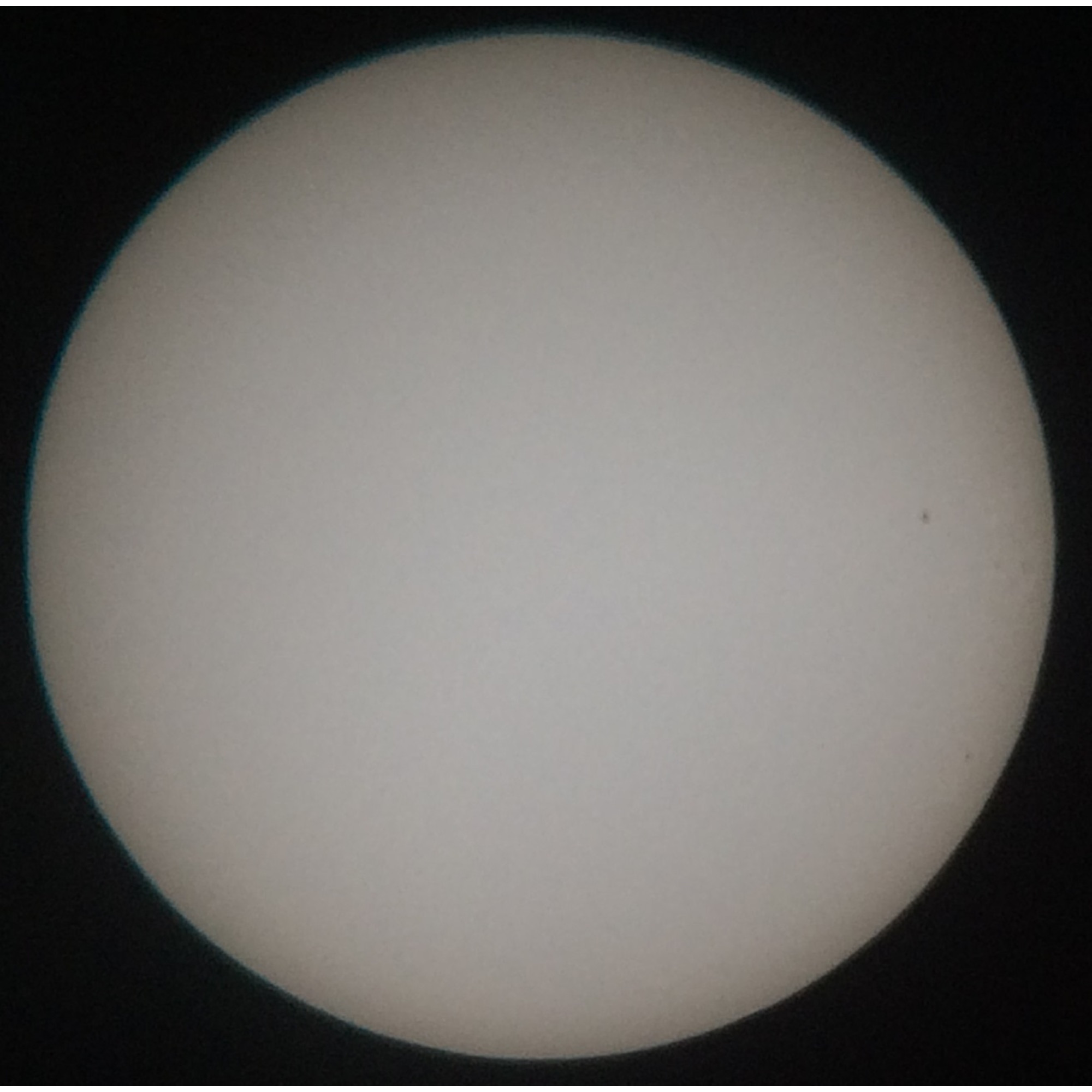 Ein heller, weißer Kreis, möglicherweise die Sonne, vor schwarzem Hintergrund. Kleiner dunkler Fleck rechts sichtbar.