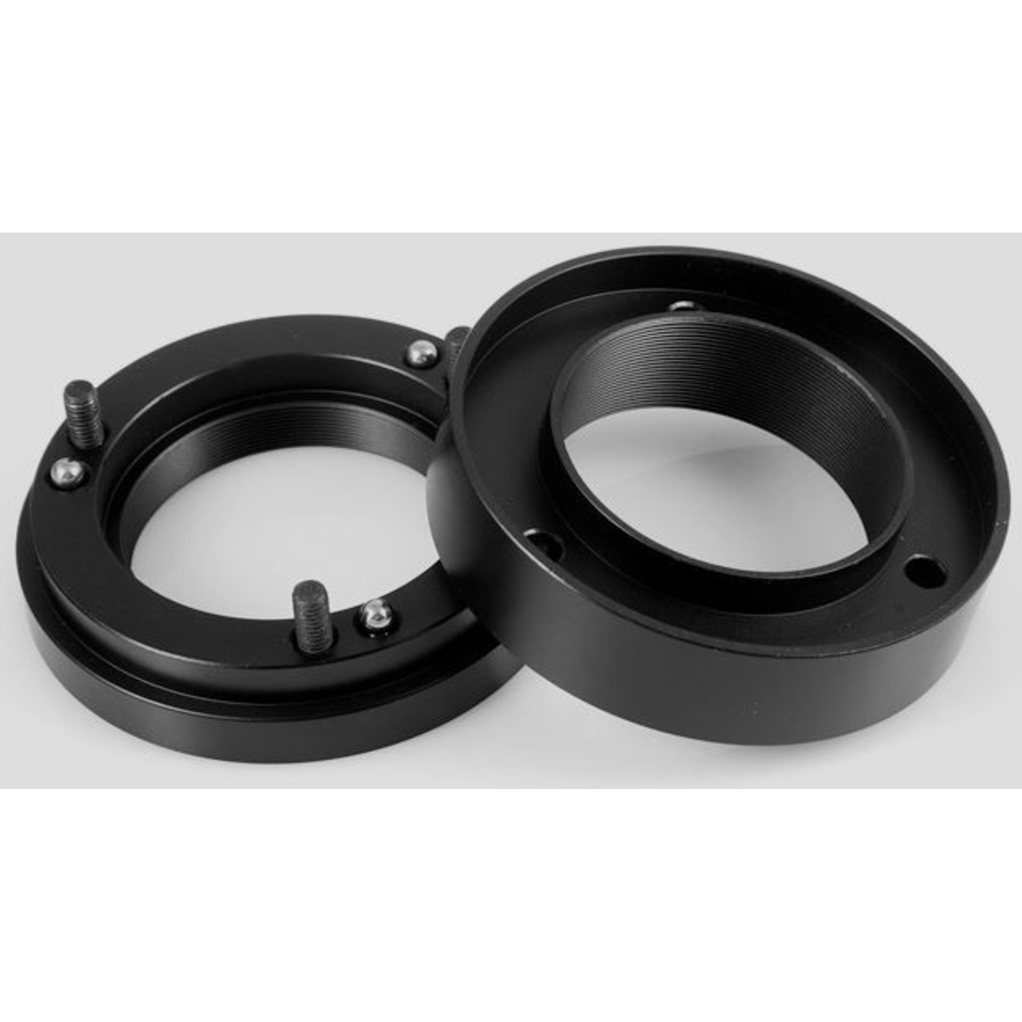 Zwei schwarze Metallringe mit Innengewinde. Ein Ring hat Schrauben. Sie liegen auf einer hellgrauen Oberfläche.