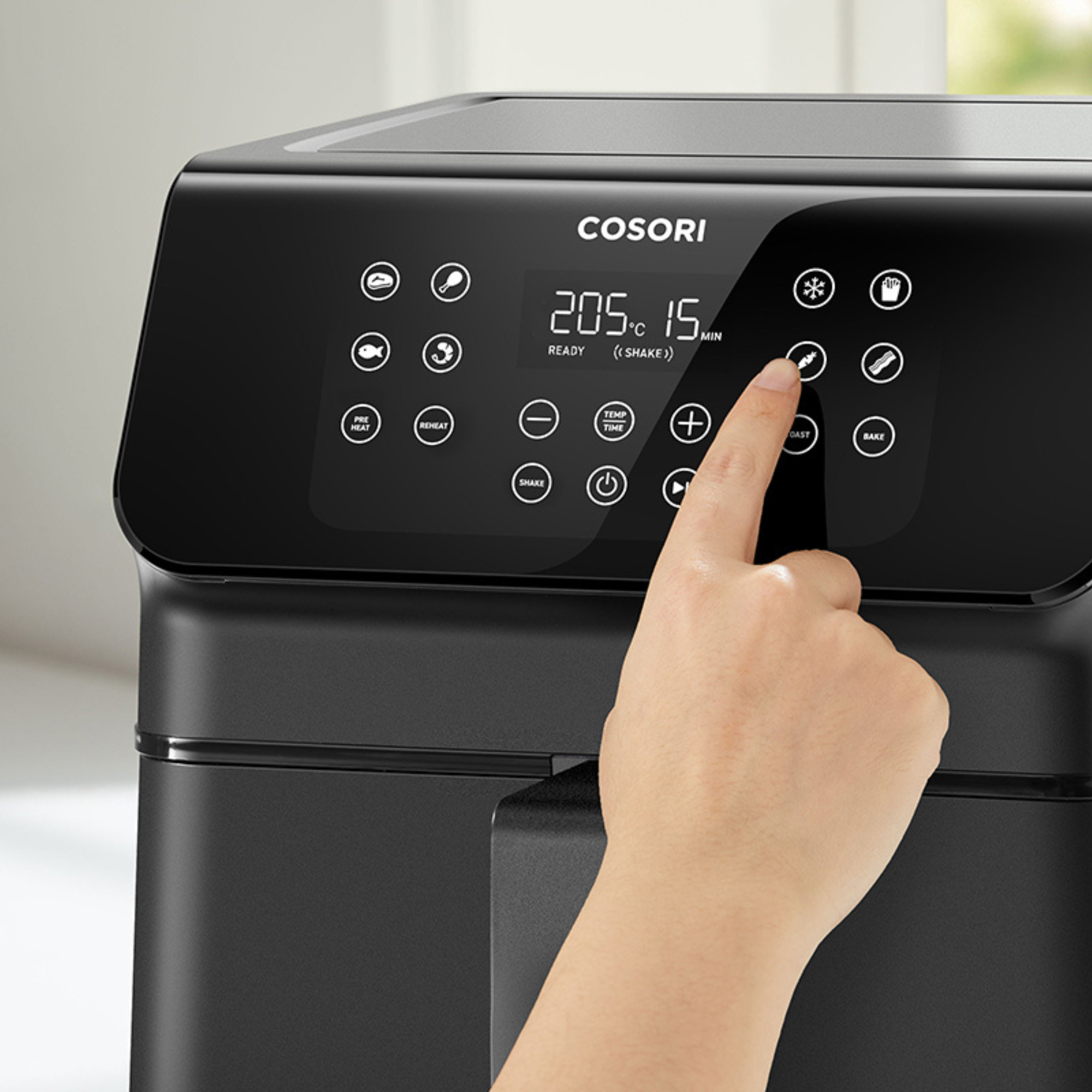 Een hand raakt het wortelpictogram op een zwarte airfryer aan. Het display toont 205°C en 15 min.
