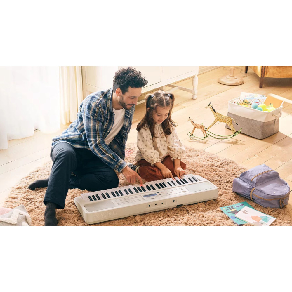 Mężczyzna i dziewczynka siedzą na dywanie i grają na keyboardzie. Zabawki i plecak w tle. Mężczyzna pokazuje.