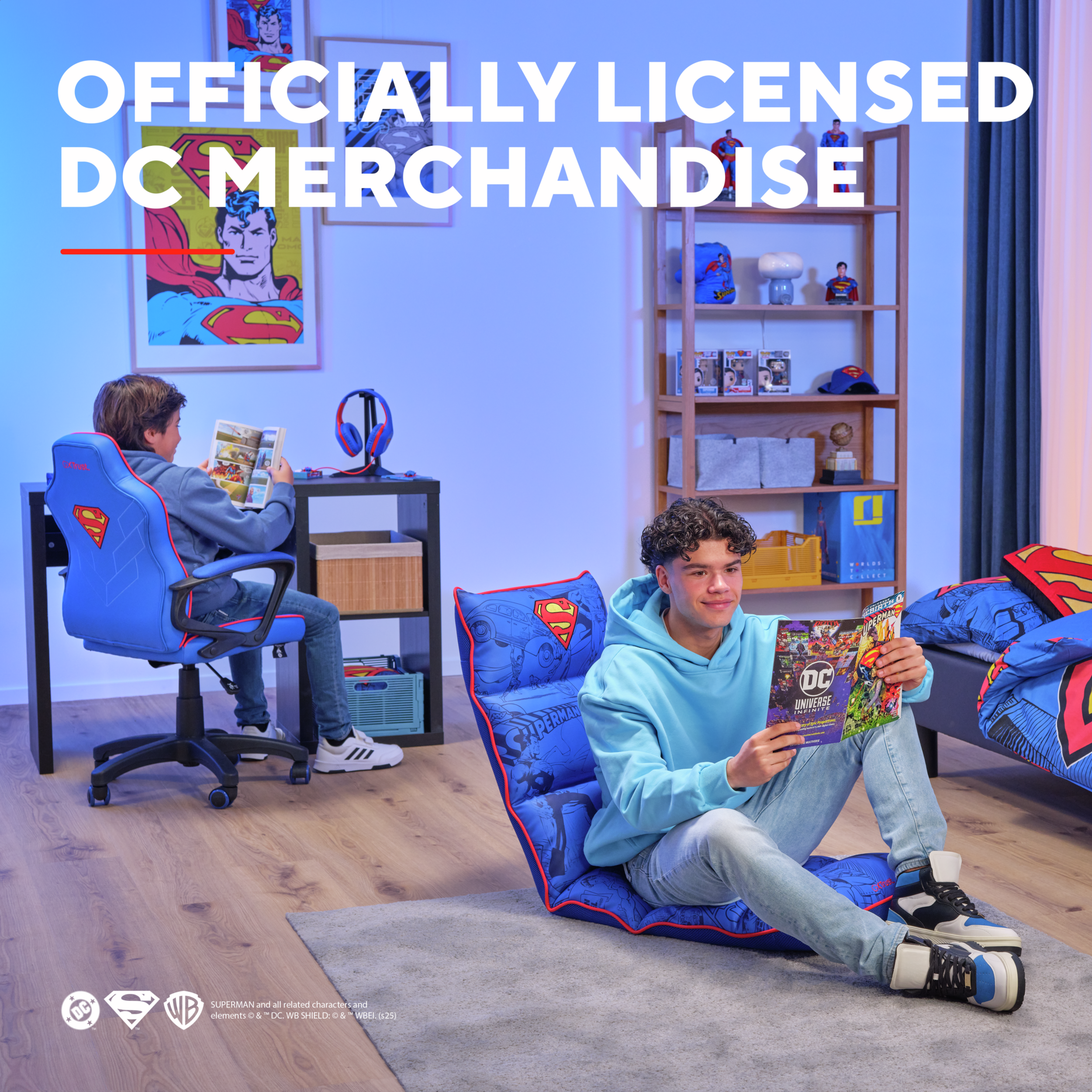 Dwóch chłopców czyta komiksy w pokoju z gadżetami DC. Jeden siedzi na niebieskim krześle, drugi na poduszce.