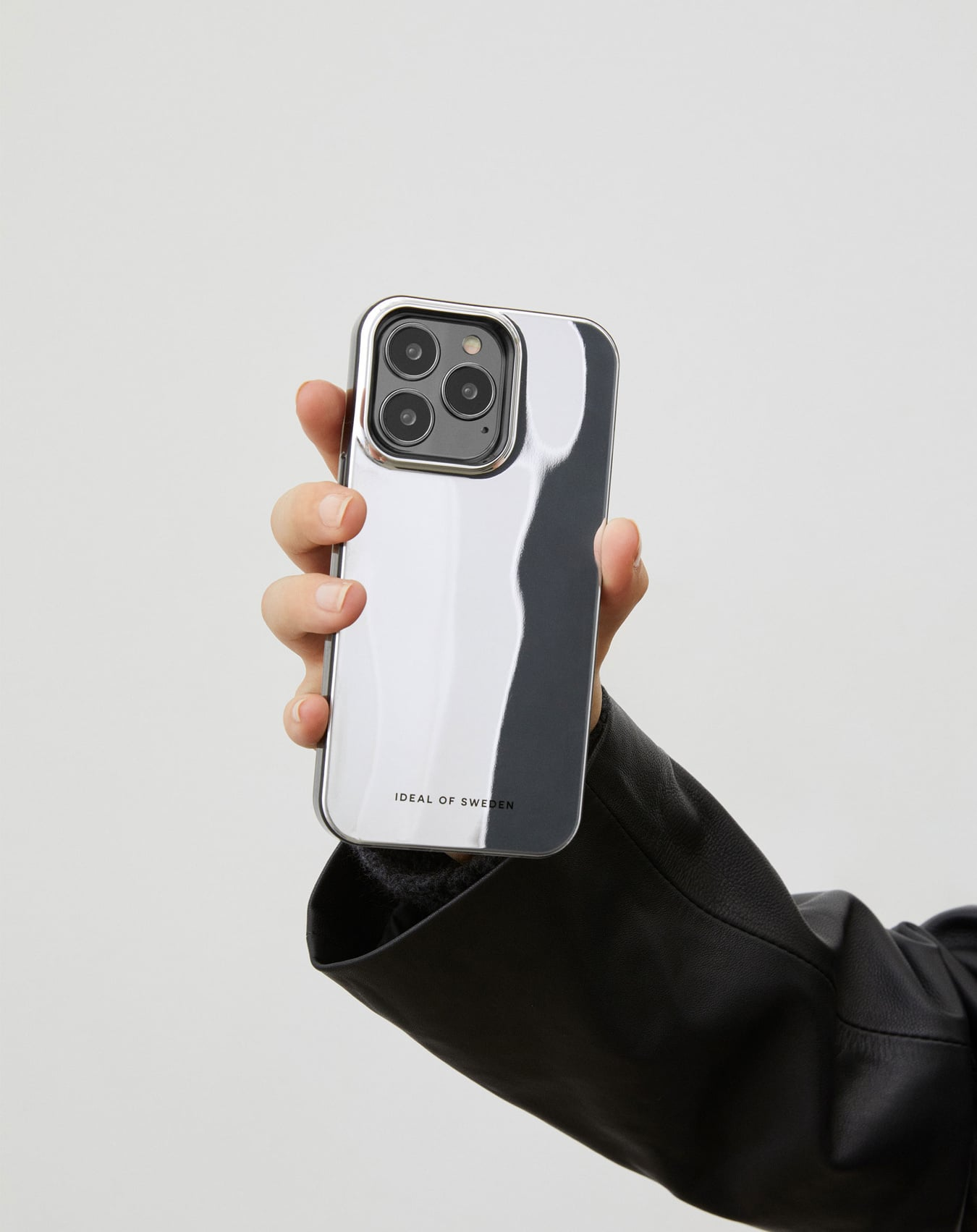 Eine Hand hält ein Telefon mit einer reflektierenden Hülle. Die Hülle hat einen silbernen Rahmen und ein schwarz-weißes Design. Der Hintergrund ist weiß.