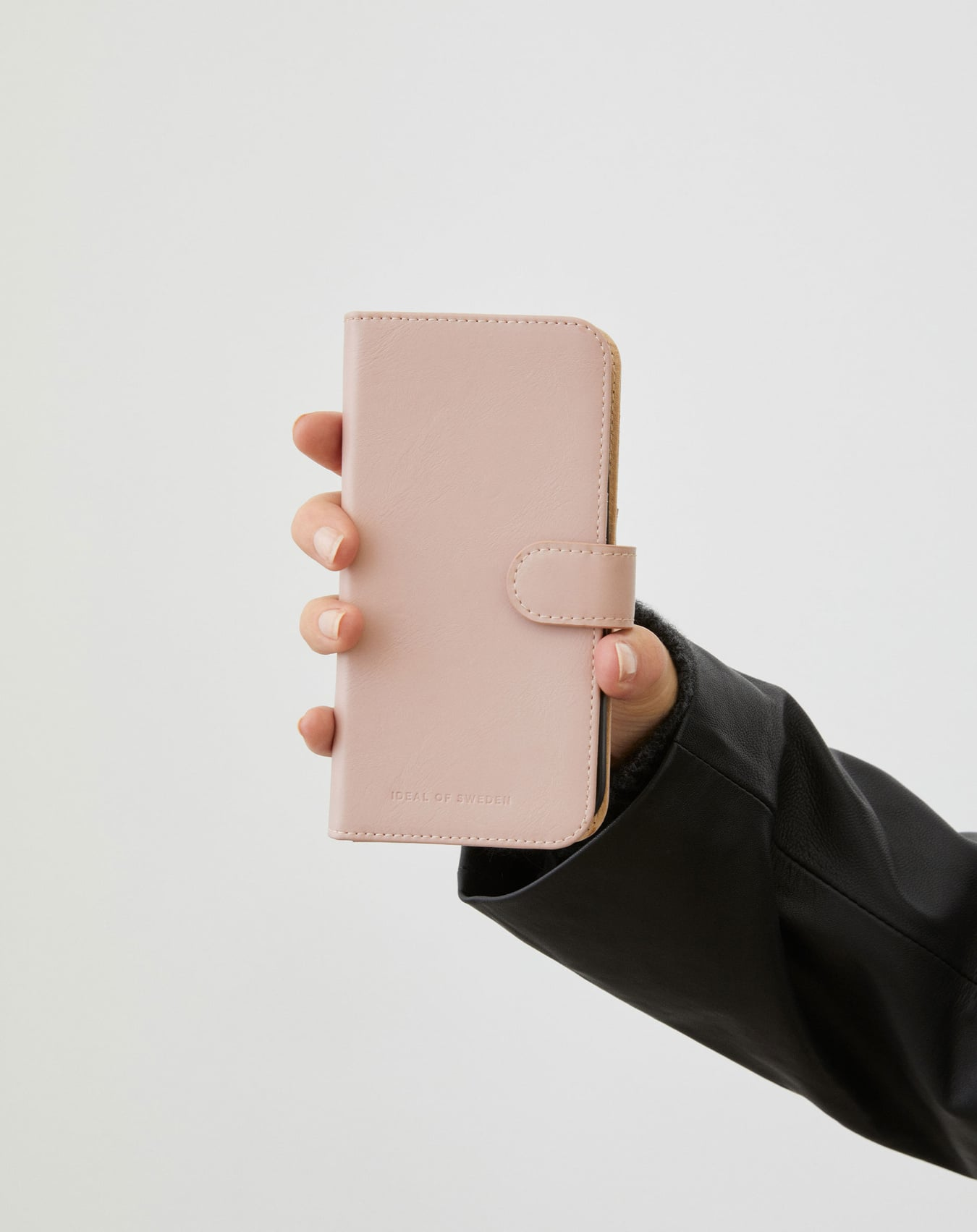 Eine Hand hält eine rosa Handyhülle mit Verschluss, Lederjacke im Hintergrund. Weißer Hintergrund.