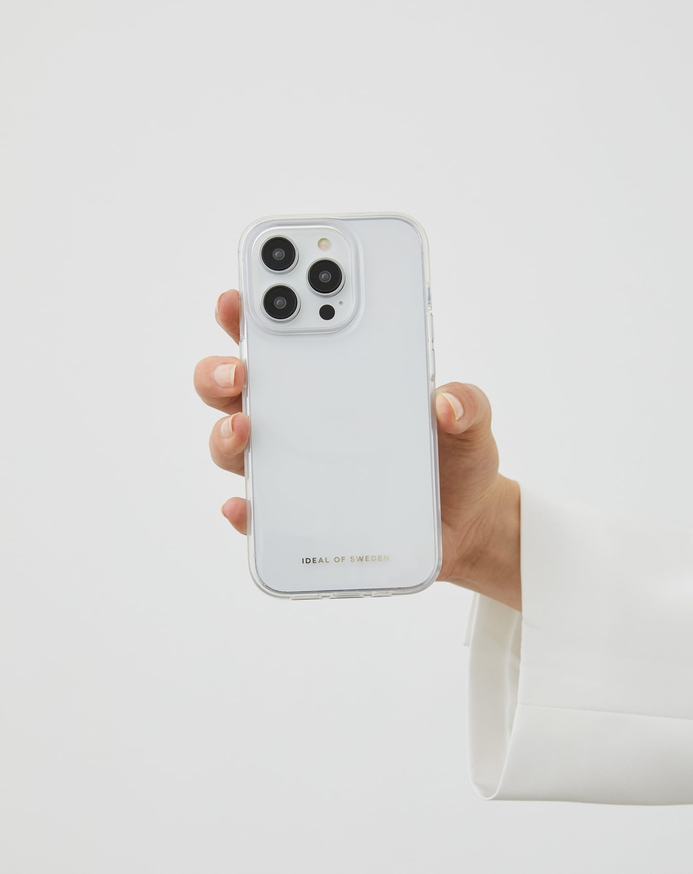 Eine Hand hält ein weißes Telefon mit einer transparenten Hülle. Das Telefon hat drei Kameralinsen. Weißer Hintergrund.