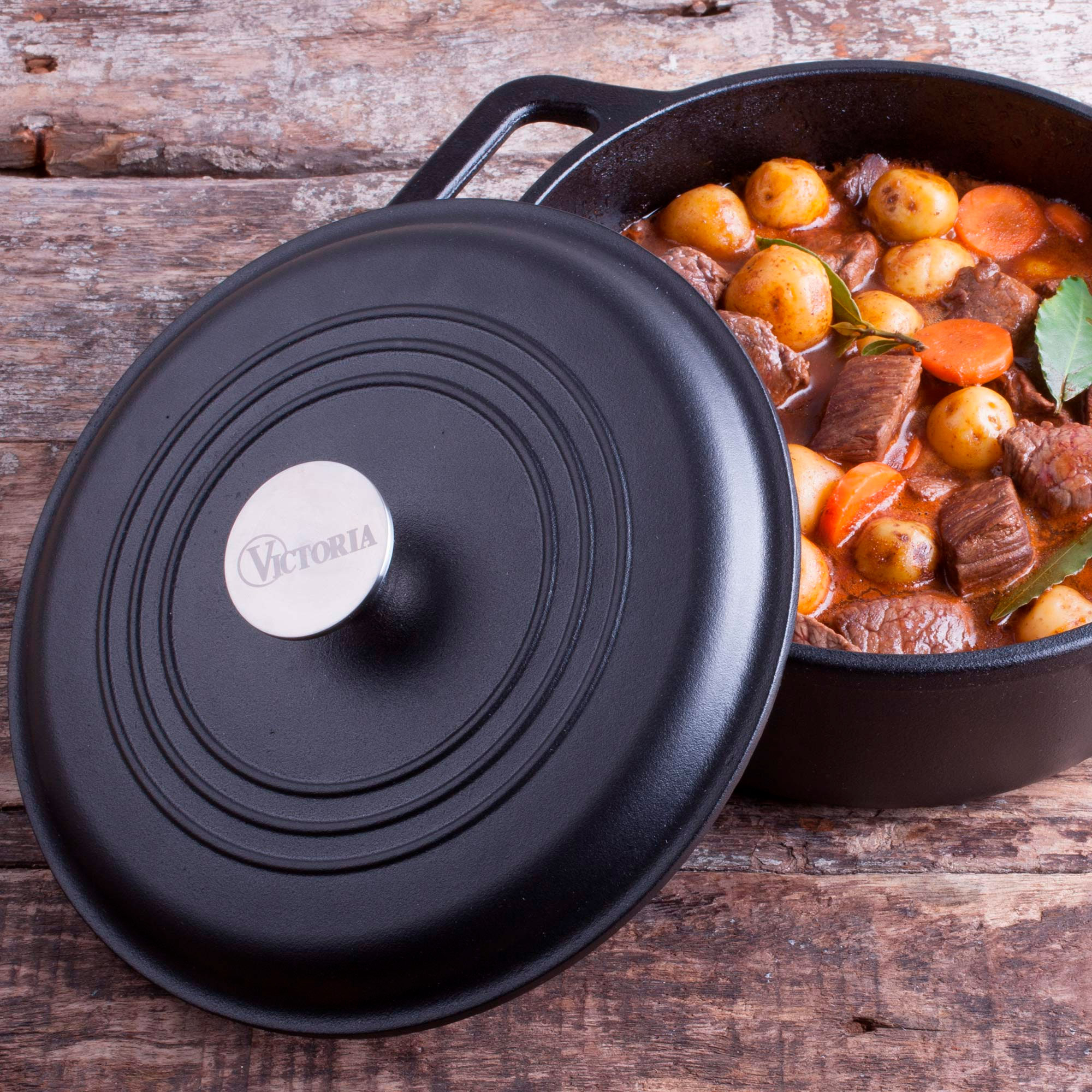 Una olla de hierro fundido con estofado adentro, con la tapa al lado. La tapa tiene la palabra Victoria.