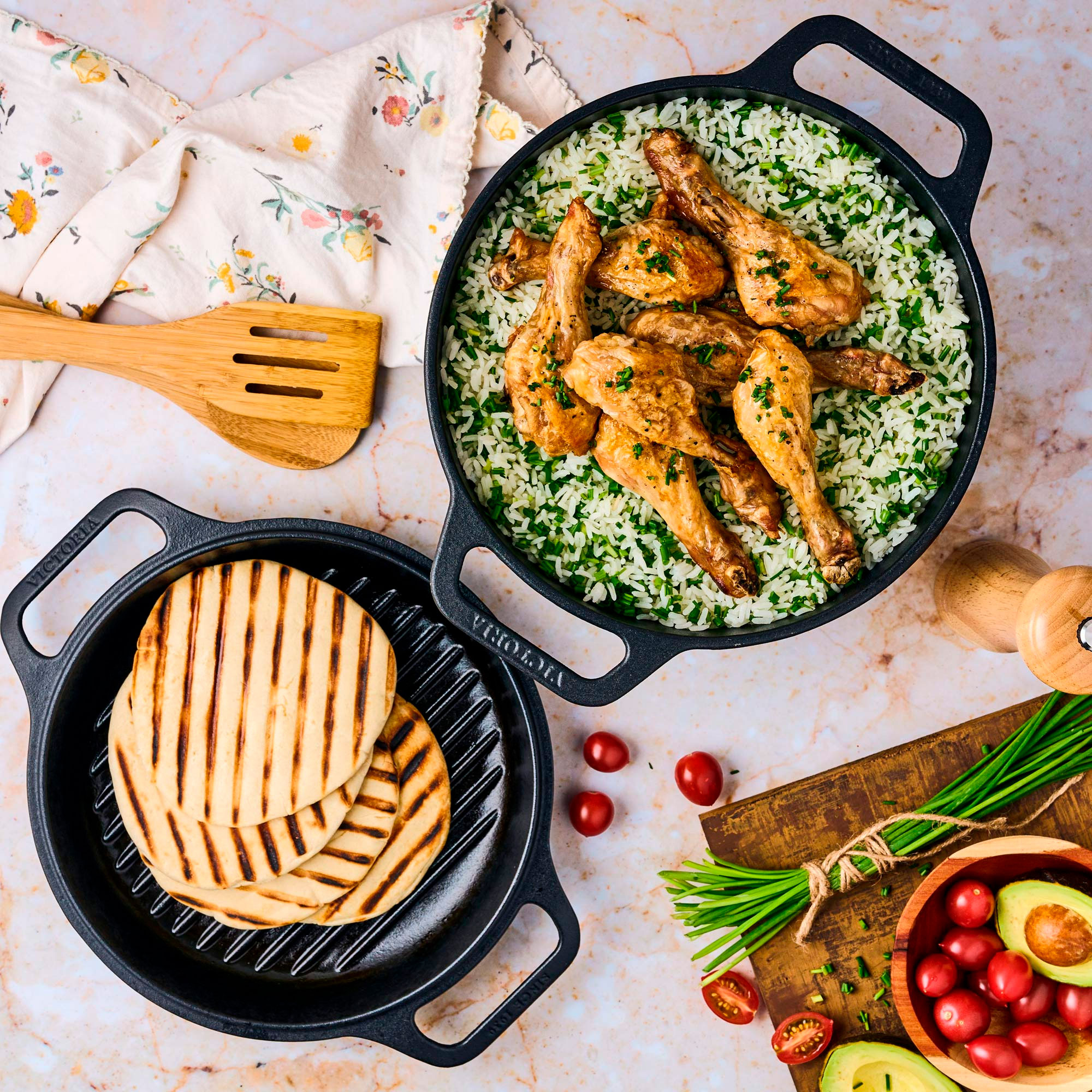 Vista aérea de una comida con muslos de pollo, arroz, pan a la parrilla, aguacate, tomates y cebollino.