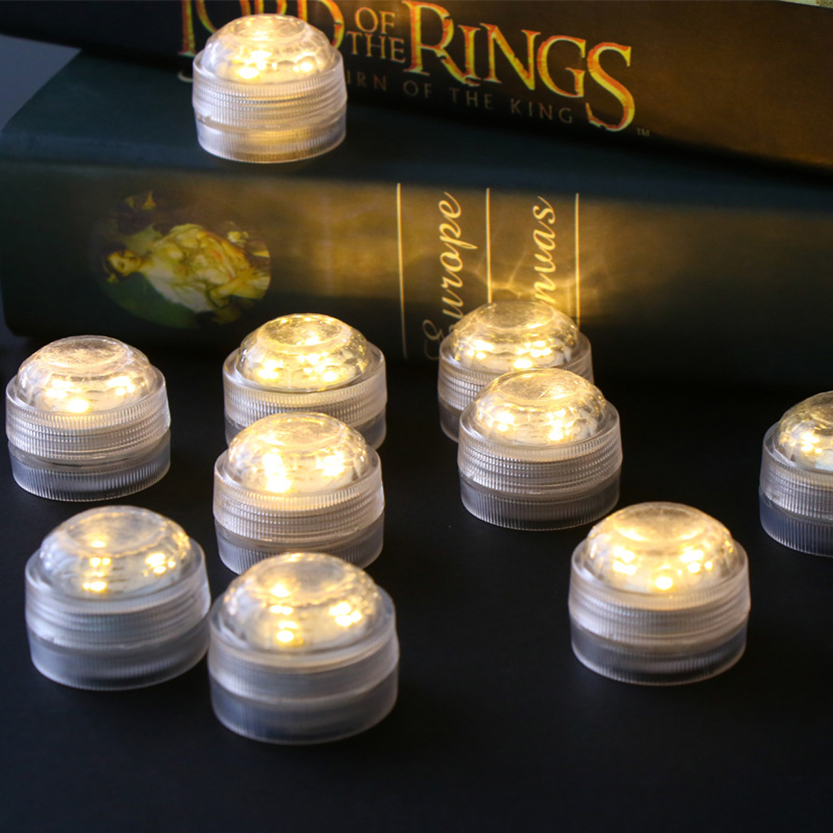Beleuchtete, klare, runde Lichter vor einem Buch. Buchtitel ist "Der Herr der Ringe". Lichter sind auf dunkler Oberfläche.