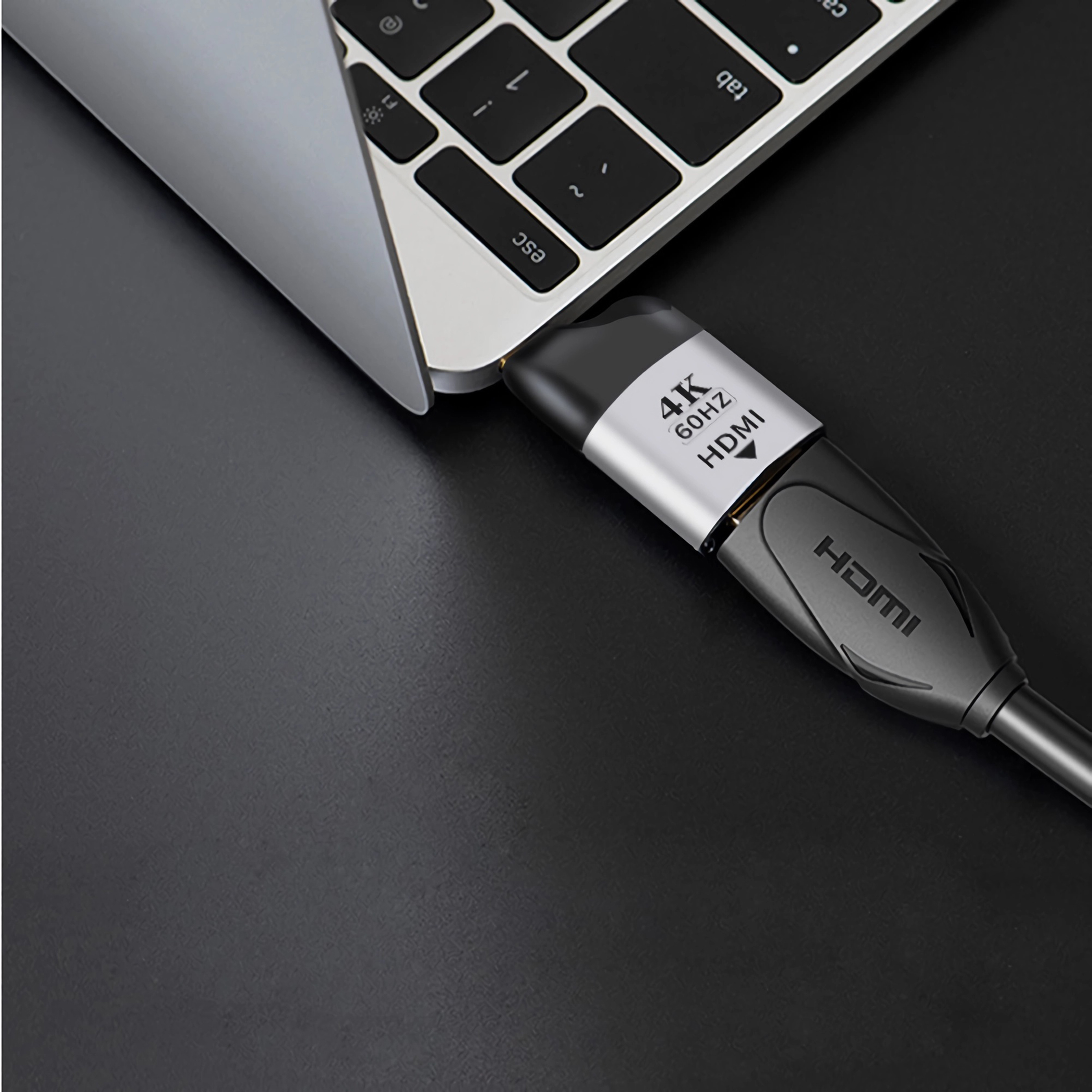 Ein HDMI-Kabel, das an einen Laptop angeschlossen ist. Das Kabel ist schwarz und silber, mit der Aufschrift '4K 60Hz HDMI'. Schwarze Oberfläche.