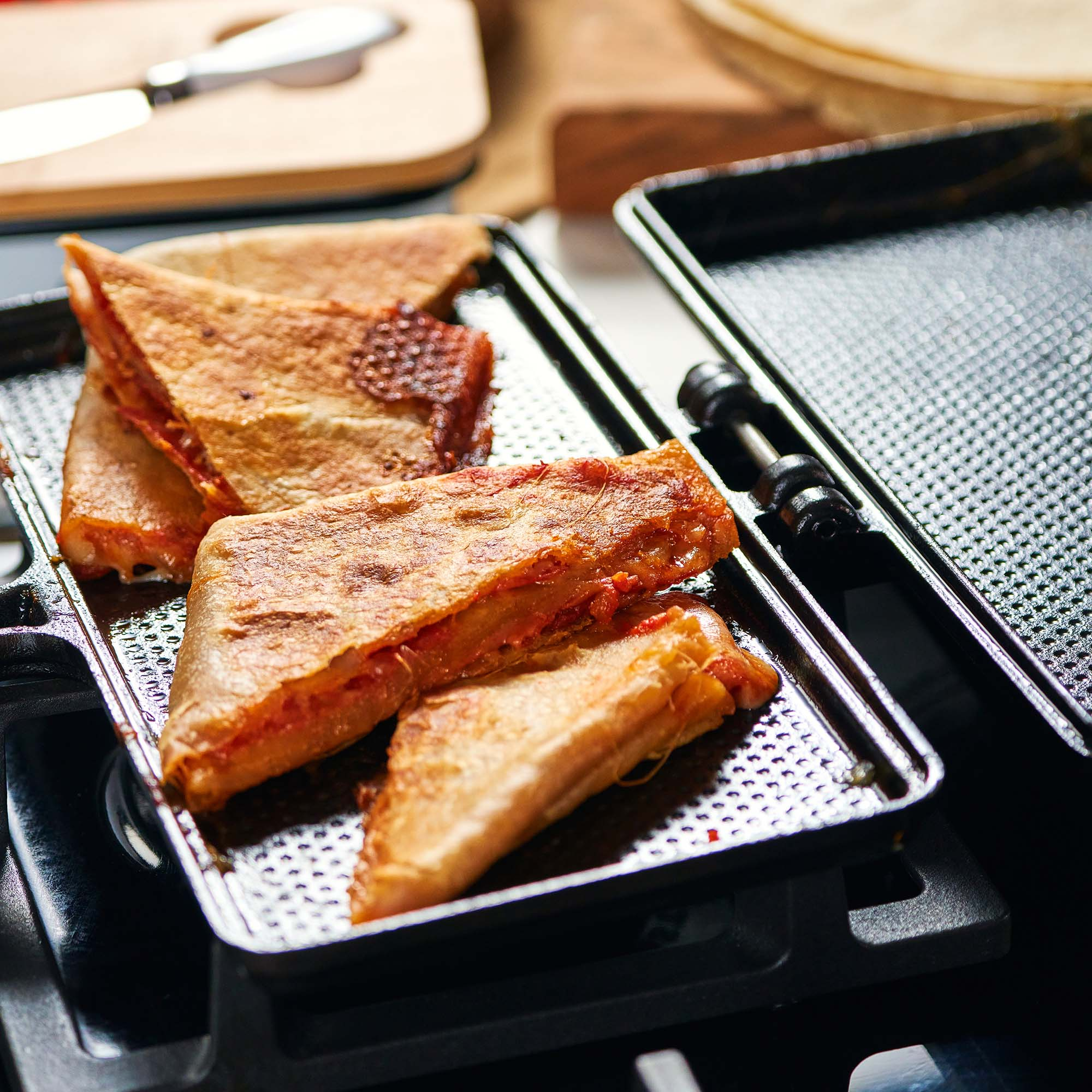 Sándwiches a la parrilla en una bandeja de metal, con un cuchillo y una tabla de cortar en el fondo.