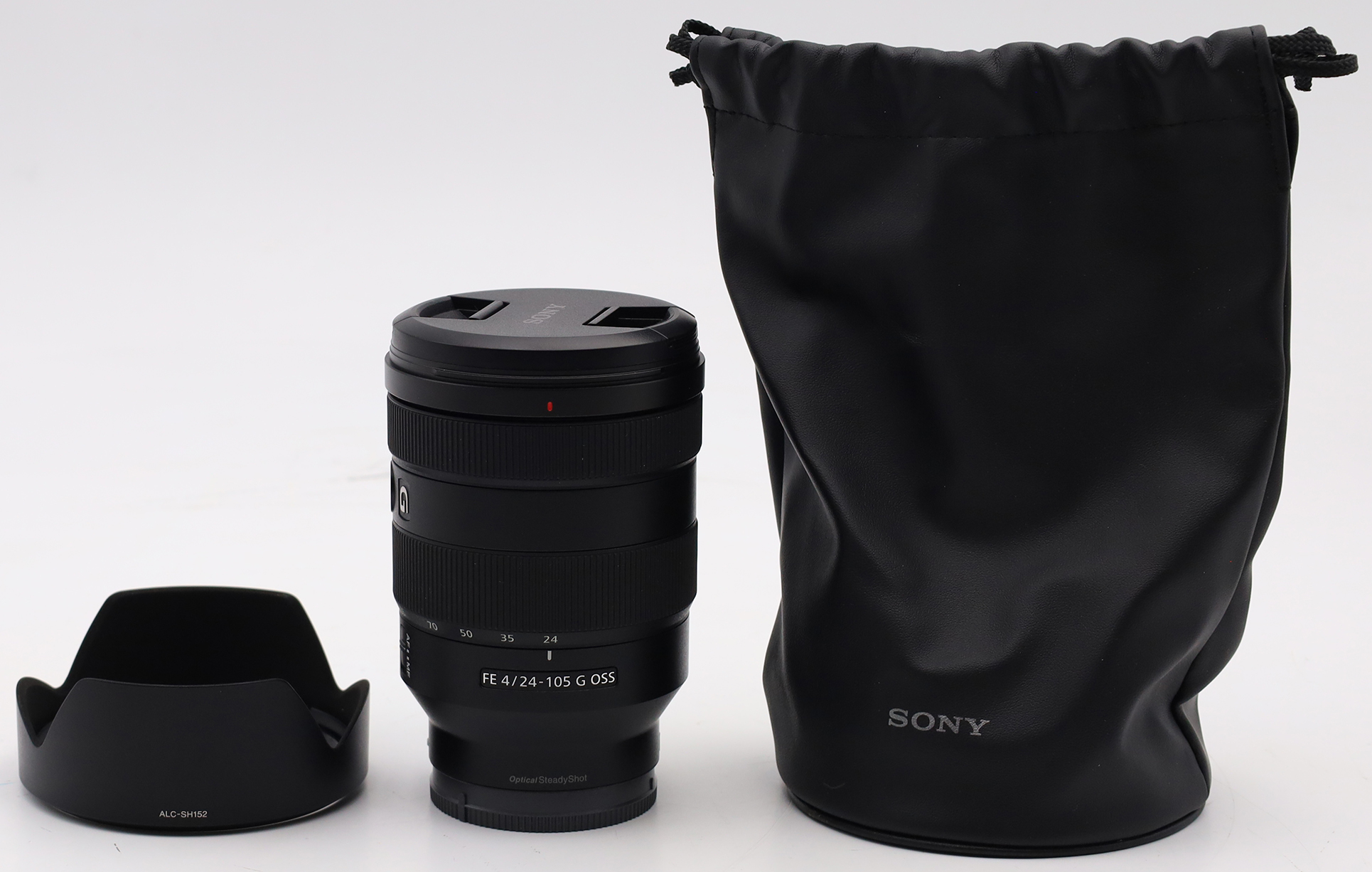 Ein schwarzes Kameraobjektiv mit Gegenlichtblende und Tasche auf weißem Untergrund. Die Objektivkappe ist auf dem Objektiv.