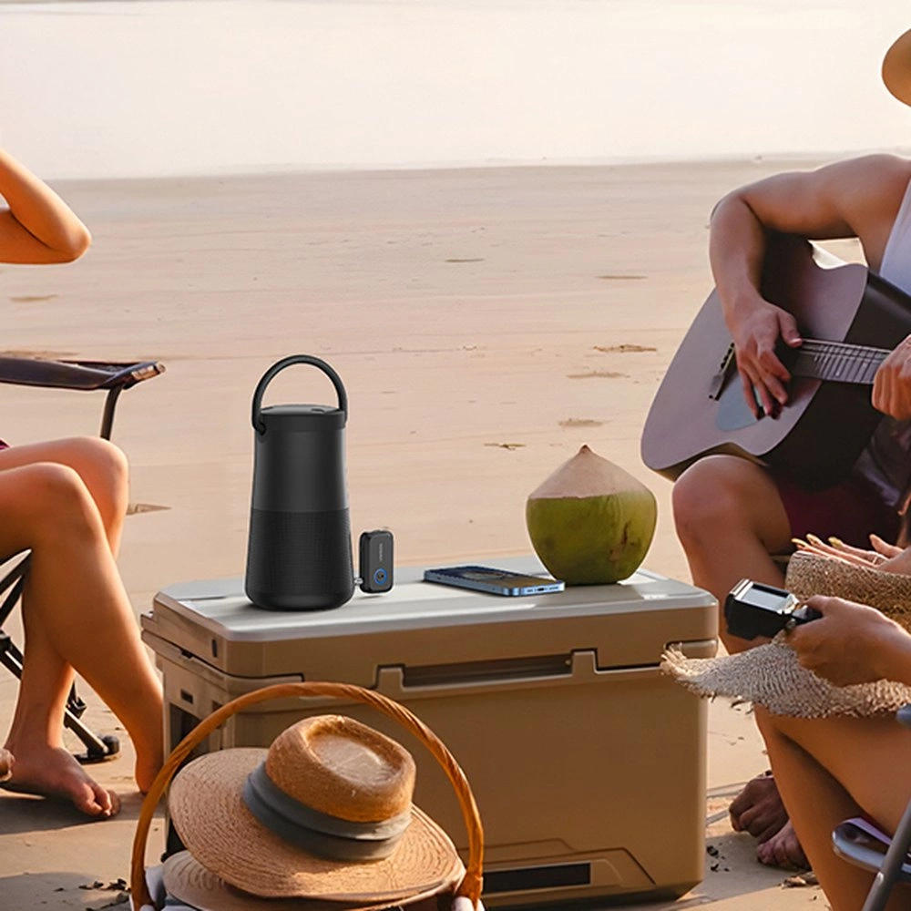 Ludzie na plaży z lodówką, głośnikiem, kokosem i gitarą. Jedna osoba gra na gitarze. Kapelusze w koszu.