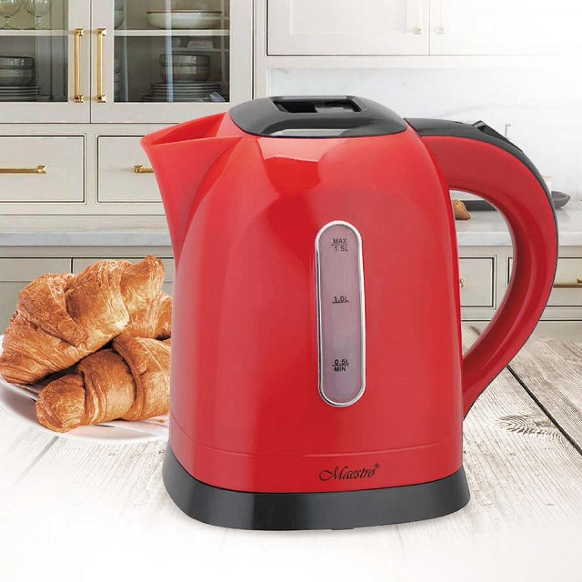 Un bollitore elettrico rosso e croissant su un piatto su un tavolo di legno. Mobili da cucina sullo sfondo.