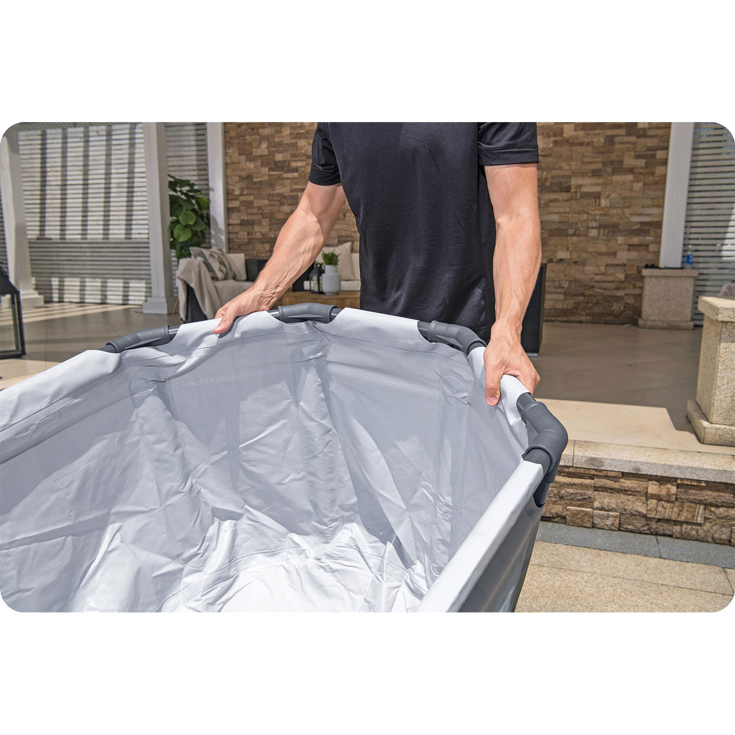 Mężczyzna trzyma duży, pusty szary pojemnik. W tle patio z ceglanymi ścianami i meblami ogrodowymi.