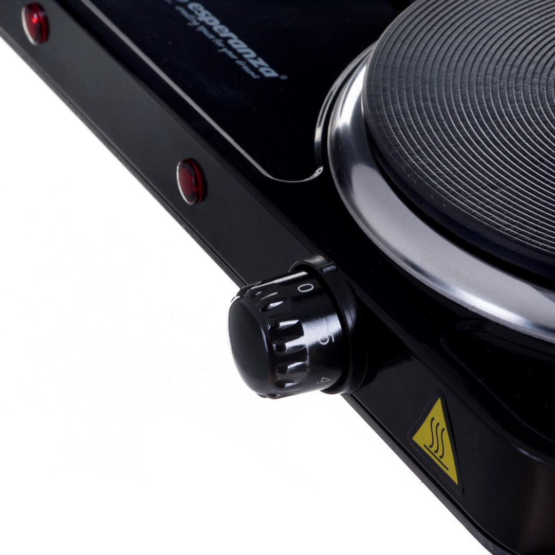 Zbliżenie czarnej kuchenki elektrycznej z pokrętłem, elementem grzejnym i czerwonymi lampkami kontrolnymi. Kuchenka na białym tle.