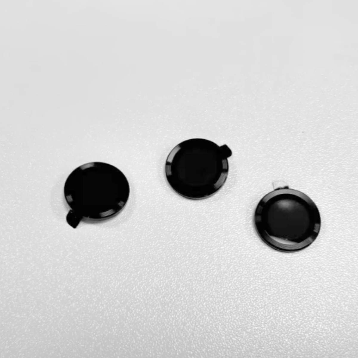 Trzy czarne, okrągłe obiekty z małymi wypustkami na białej powierzchni. Obiekty są ułożone w trójkąt.