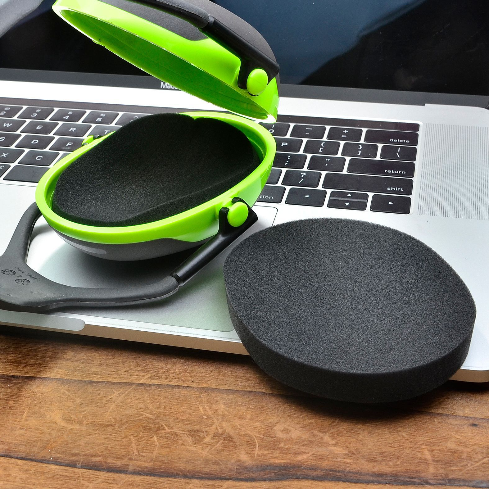 Zielono-czarny zestaw nausznników leży na laptopie. Jeden nausznik jest odłączony. Laptop stoi na drewnie.