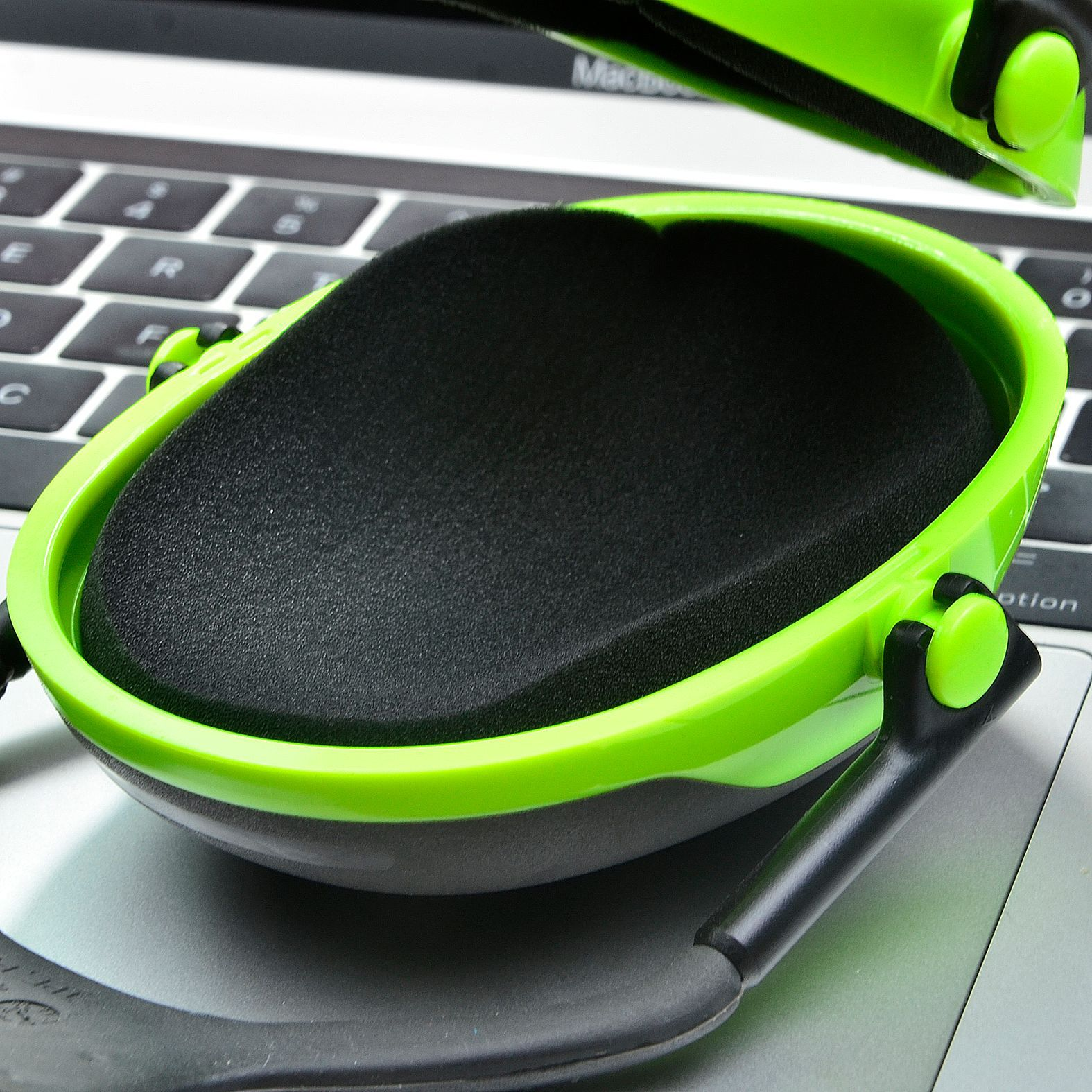 Zielone i czarne nauszniki na klawiaturze laptopa. Muszla uszna jest otwarta, odsłaniając czarną piankową wyściółkę.