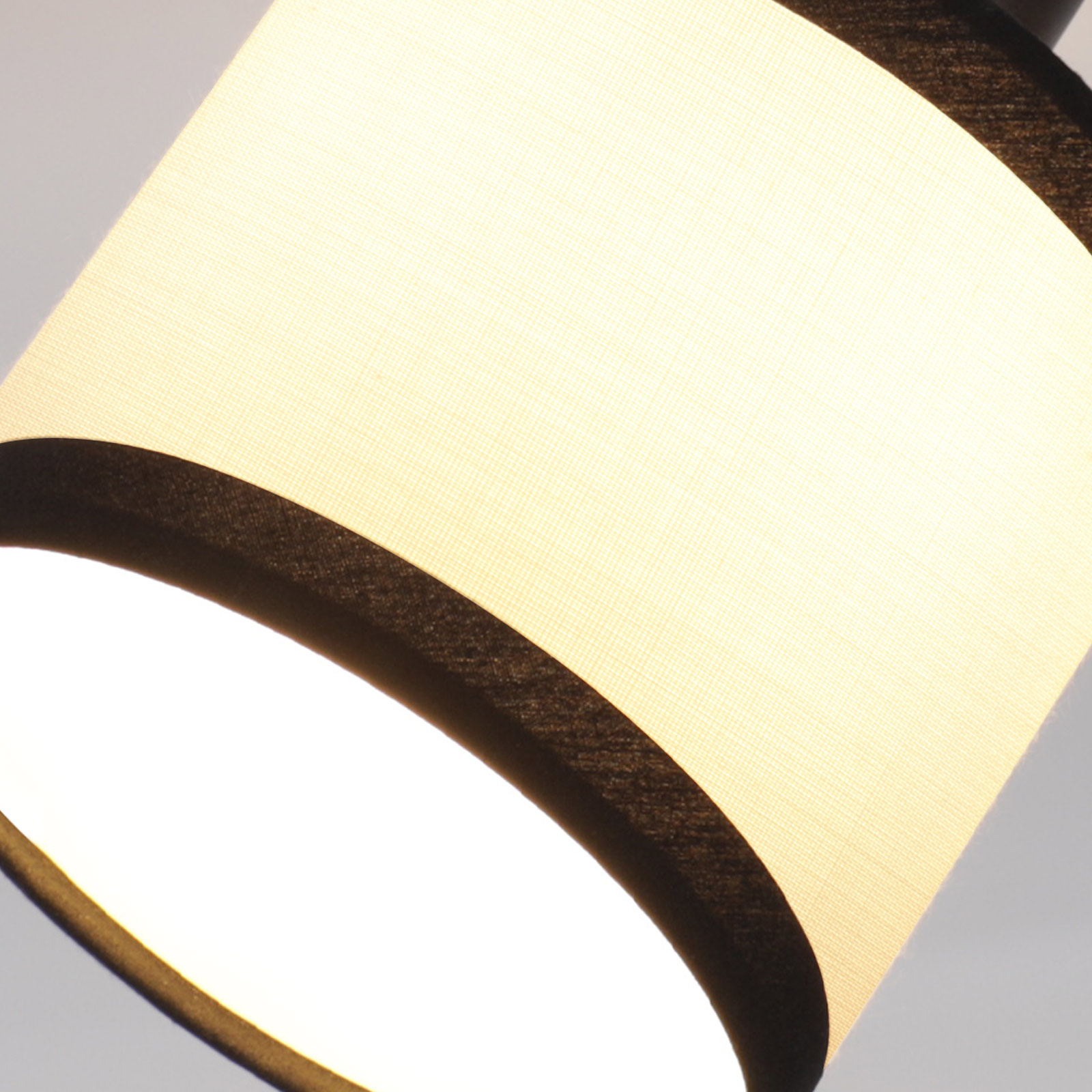 Nahaufnahme eines Lampenschirms. Er hat eine cremefarbene Innenseite und eine schwarze Zierleiste, helles Licht von unten.