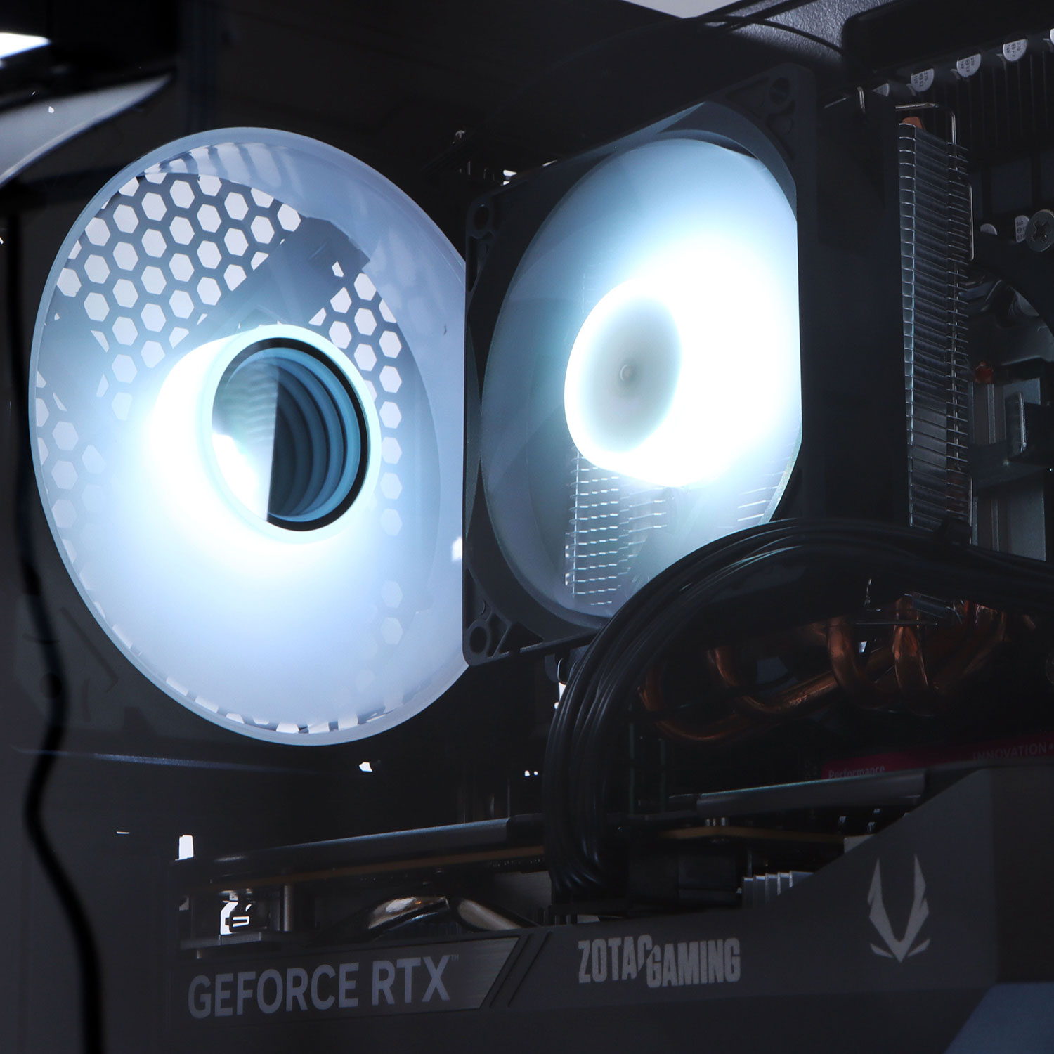 In einem Computergehäuse sind zwei helle Lüfter zu sehen. Unten ist eine Grafikkarte mit "Zotac Gaming" zu sehen.