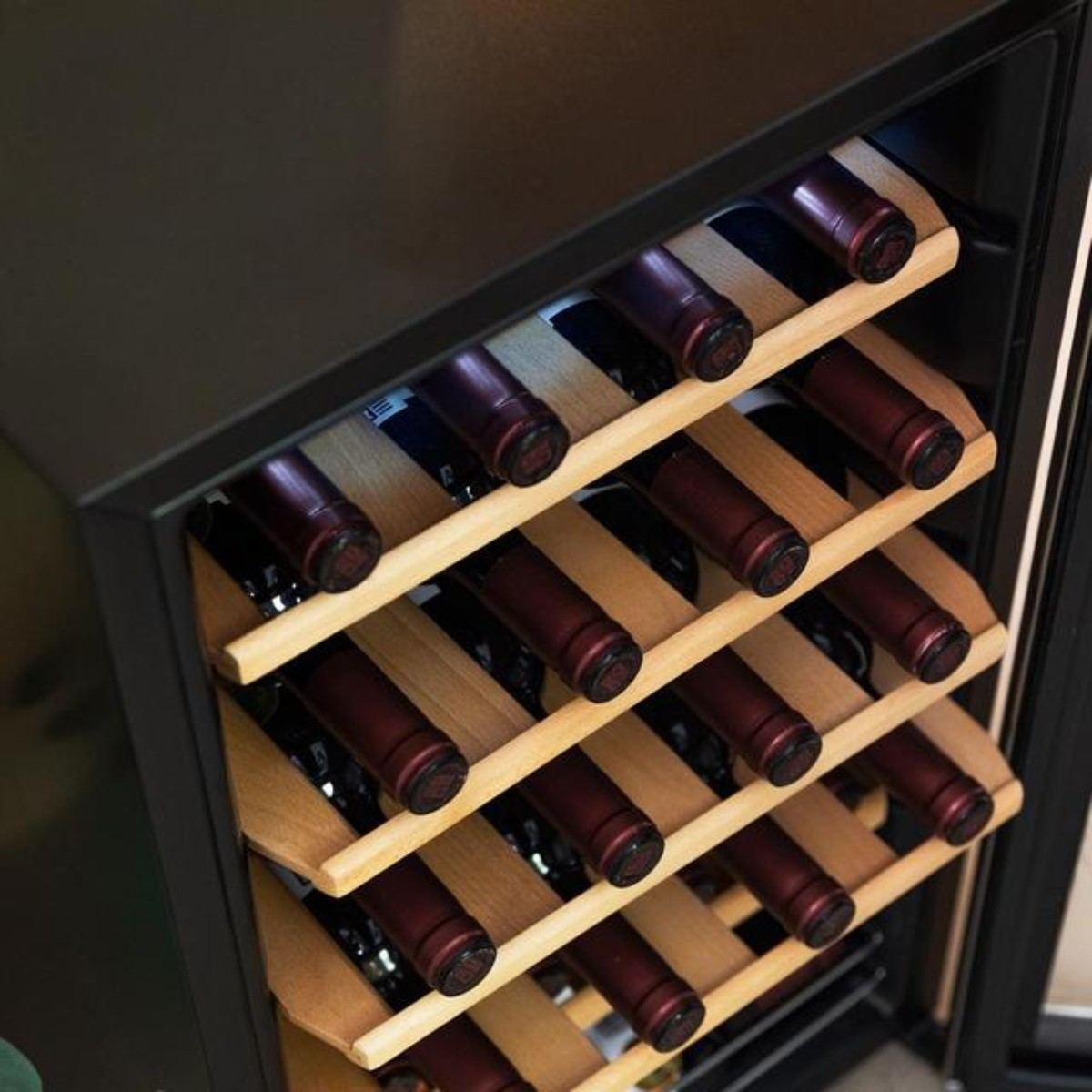 Chłodziarka do wina wypełniona butelkami wina. Butelki są czerwone i przechowywane na drewnianych półkach.