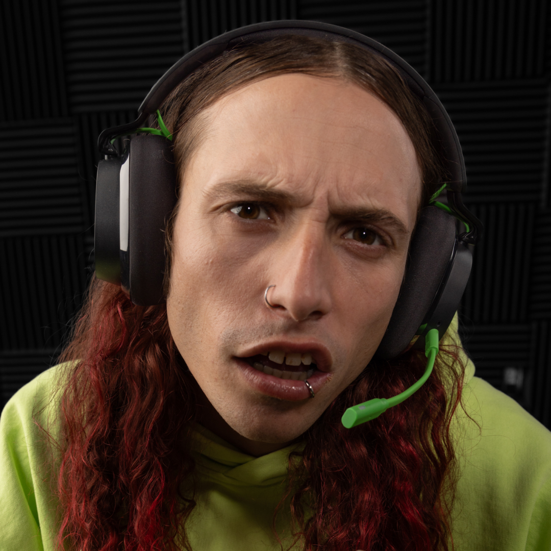 Una persona con capelli rossi e piercing indossa delle cuffie e una felpa con cappuccio verde. Sembrano sorpresi.