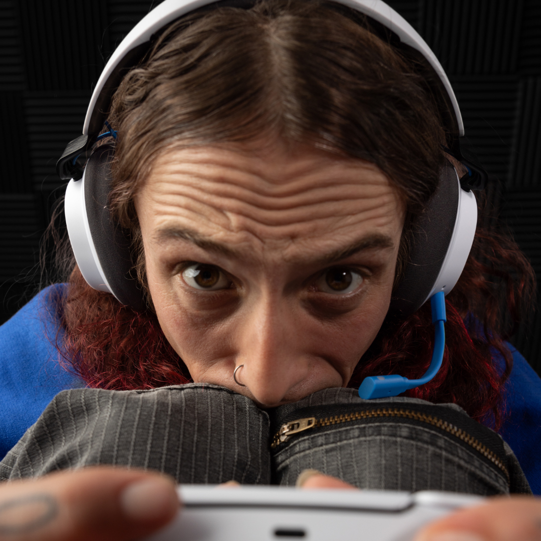 Una persona con auriculares mira fijamente. Sostiene un dispositivo blanco. El fondo es negro y lleva una camisa azul.