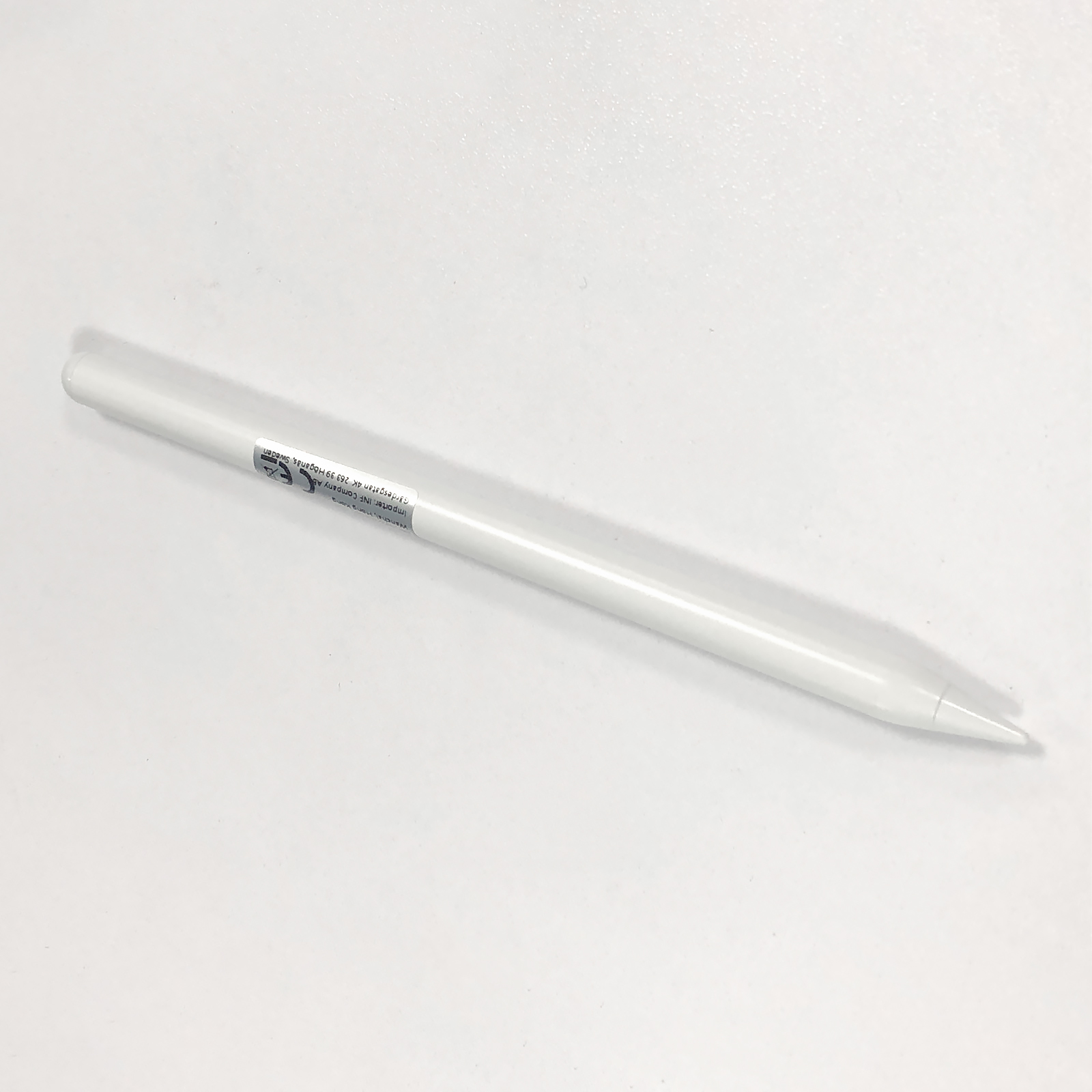 Biały rysik leży po przekątnej na białej powierzchni. U góry znajduje się etykieta. Końcówka rysika jest ostra.