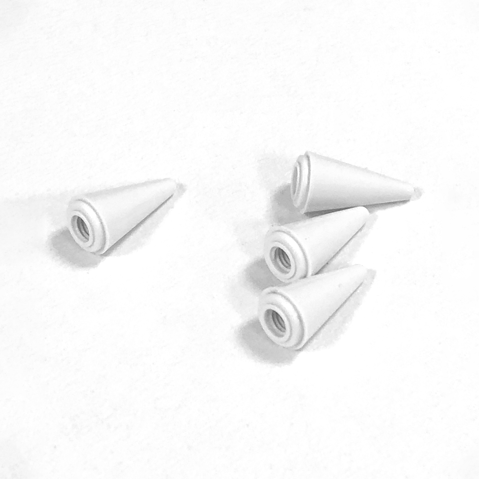 Cztery białe, stożkowe obiekty z gwintowanymi otworami na białej powierzchni. Jeden izolowany, inne zgrupowane.