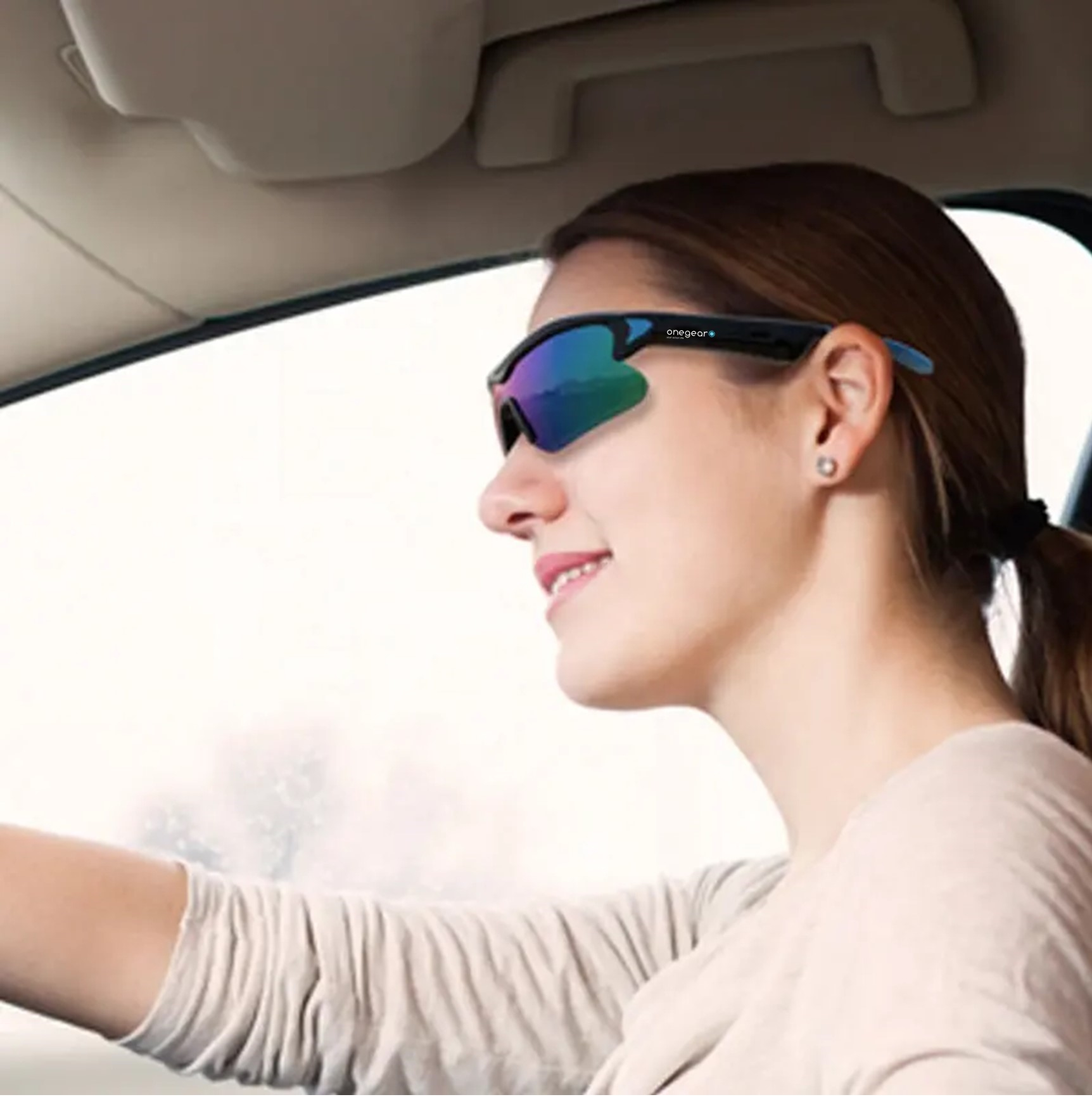 Donna con occhiali da sole in auto, sorridente. Gli occhiali hanno una tinta blu e indossa una camicia beige.