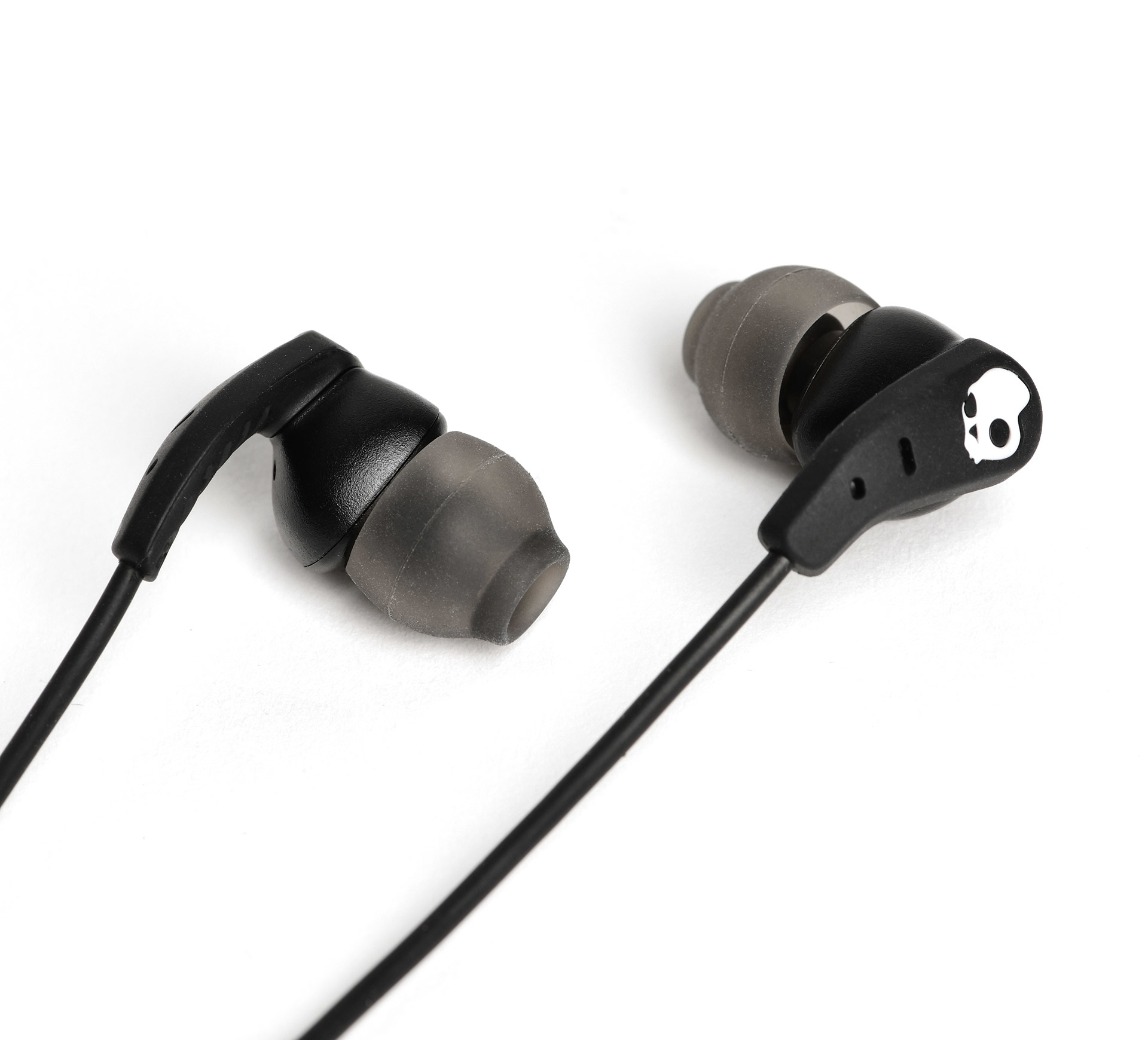 Schwarze Skullcandy-Ohrhörer auf weißem Hintergrund. Ein Ohrhörer hat ein Totenkopf-Logo.