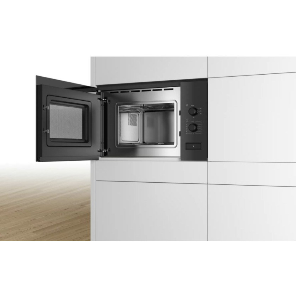 Nowoczesna kuchenka mikrofalowa jest wbudowana w białe szafki. Drzwi są otwarte, odsłaniając wnętrze. Drewniana podłoga na pierwszym planie.