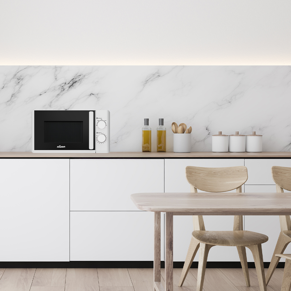 Un microondas blanco con puerta negra está sobre una encimera. Cocina con armarios blancos, salpicadero de mármol y mesa de madera.