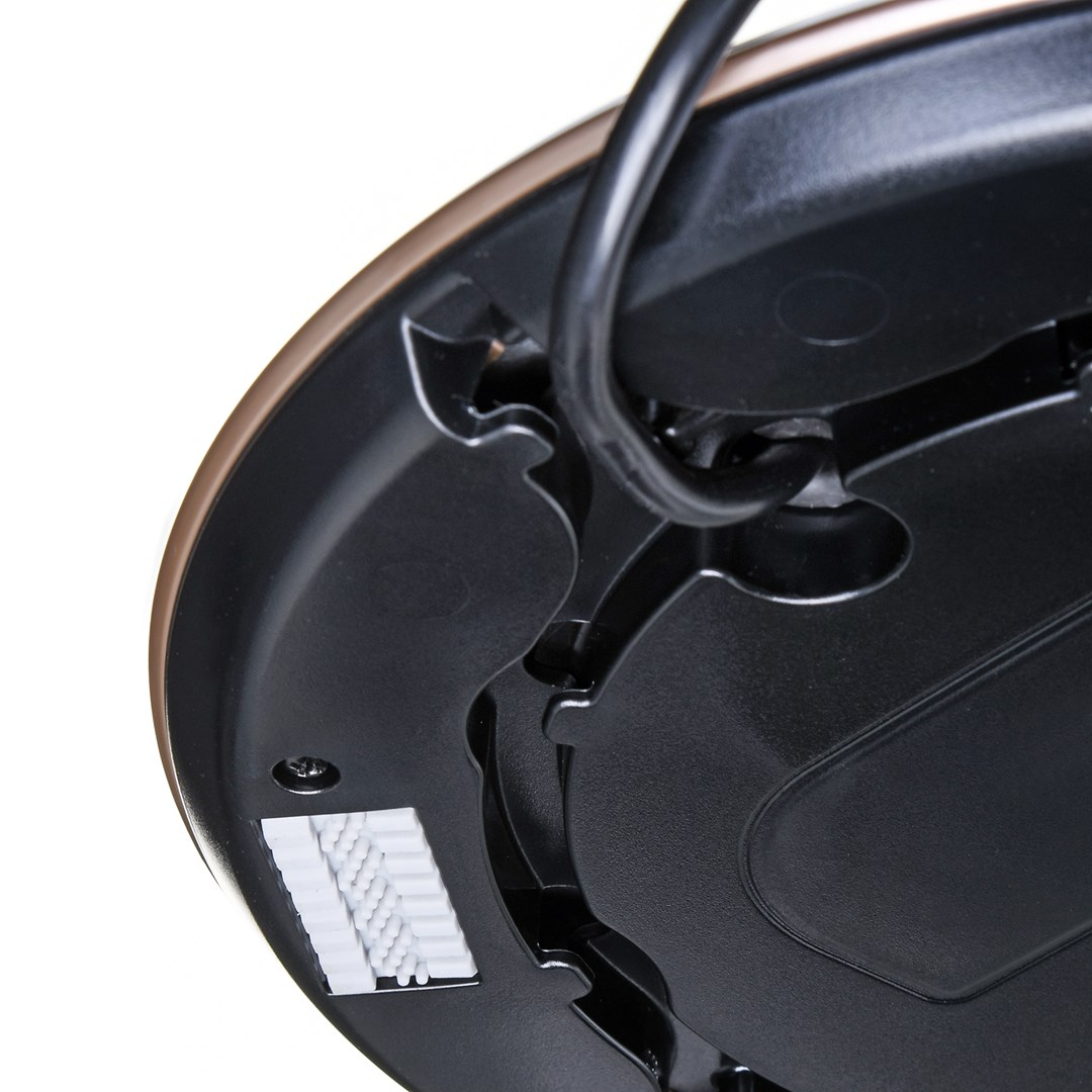 Zbliżenie czarnej podstawy urządzenia z brązową krawędzią. Czarny przewód wygina się nad nią. Biały, prostokątny element jest zamocowany.