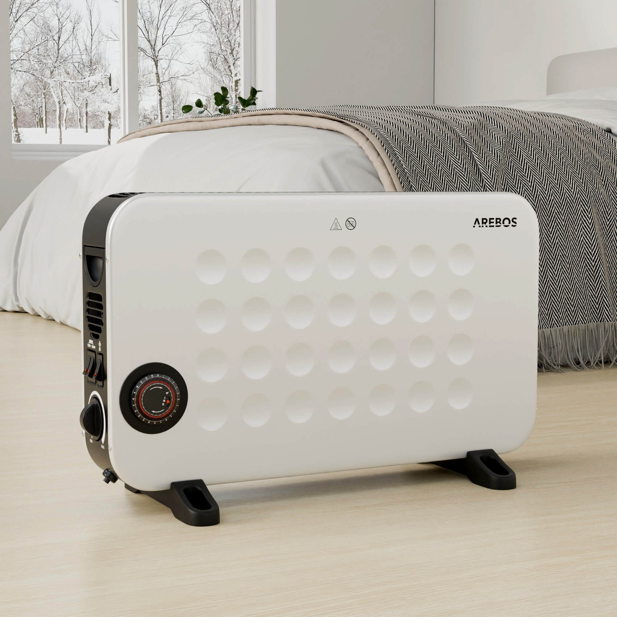 Ein weißer Arebos-Heizlüfter steht in einem Raum. Ein Fenster zeigt eine schneebedeckte Szene im Freien. Ein Bett mit Decke im Hintergrund.